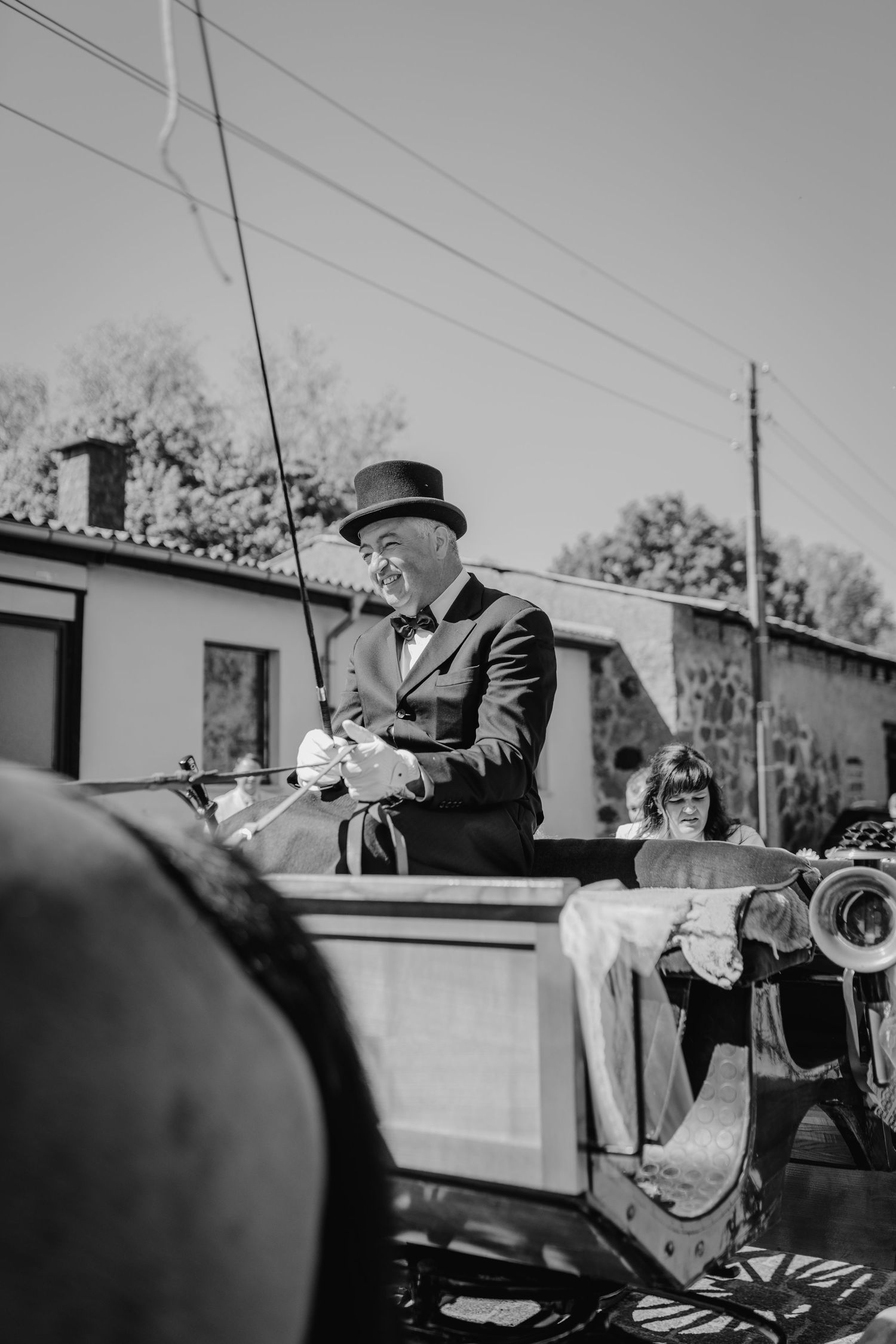 A vintage black and white photo of a coachman in formal attire driving a horse-drawn carriage.
