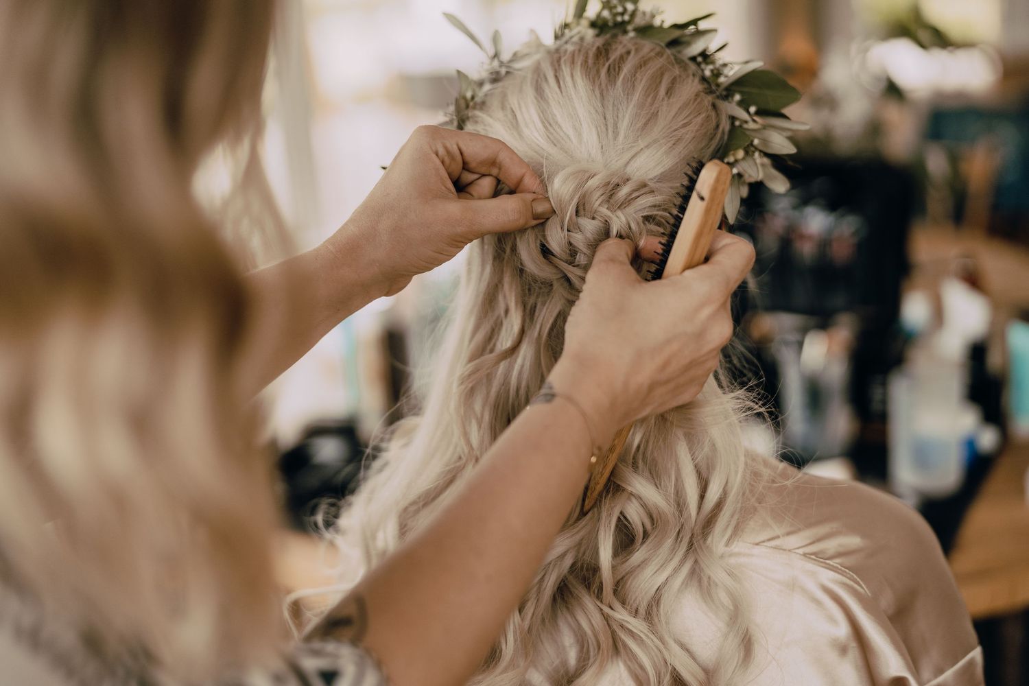 Hands styling a delicate floral crown on light hair during wedding preparations.