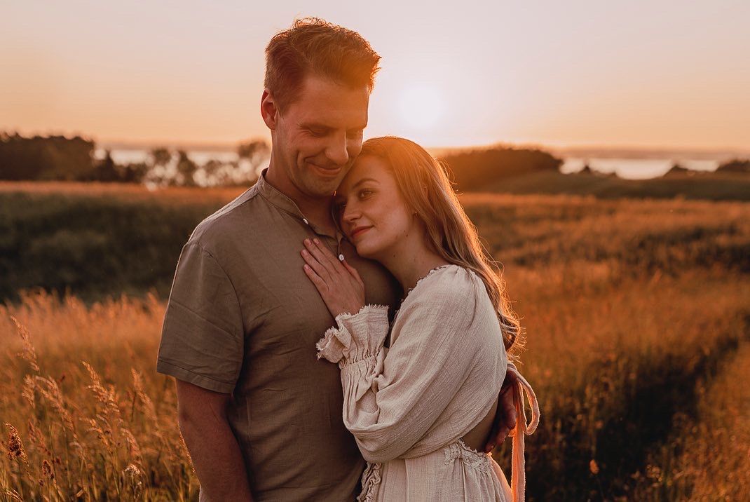 A couple shares a tender embrace in a golden sunset field of tall grass and wildflowers.