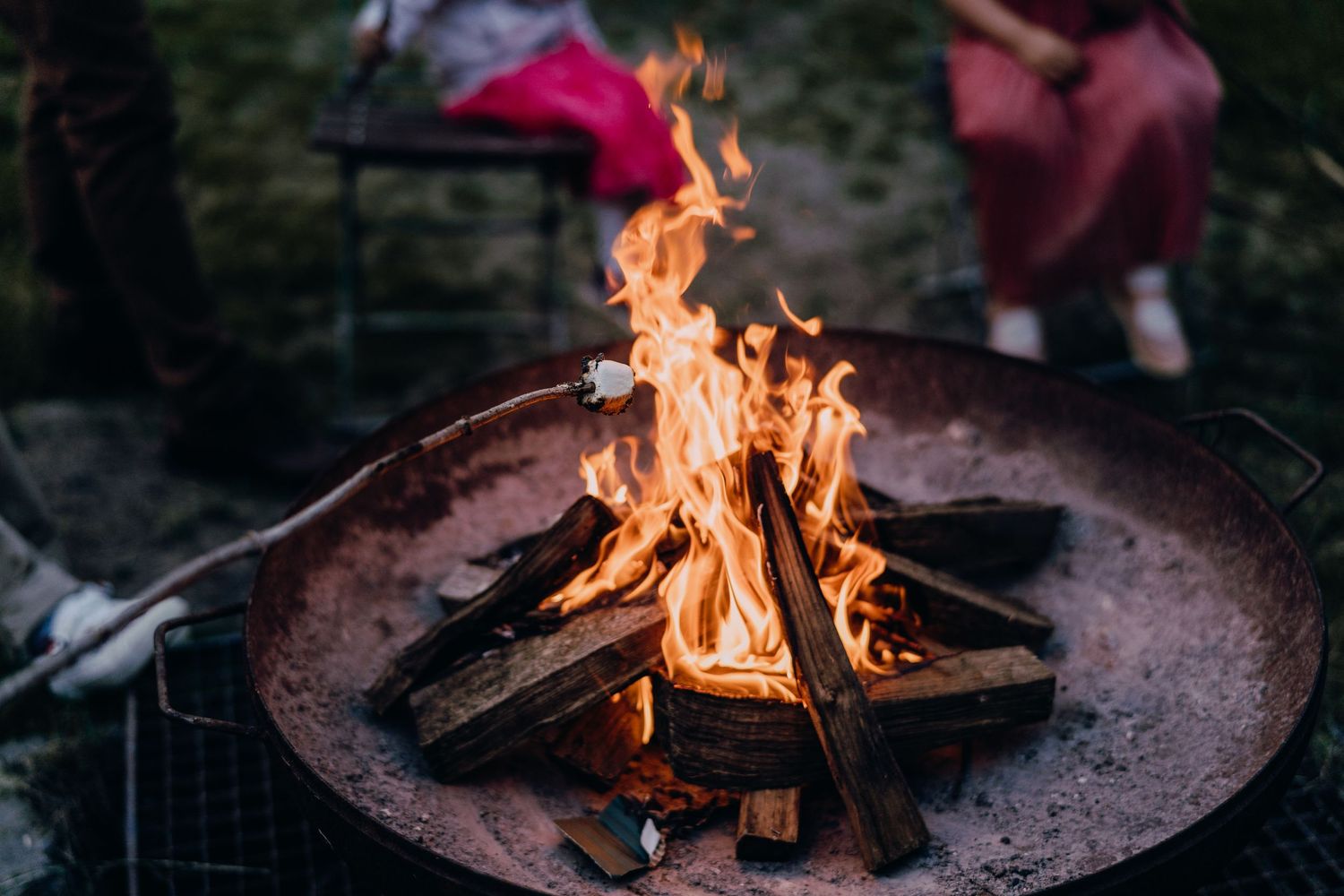 Roaring campfire in a metal fire pit with bright orange flames against dark background.