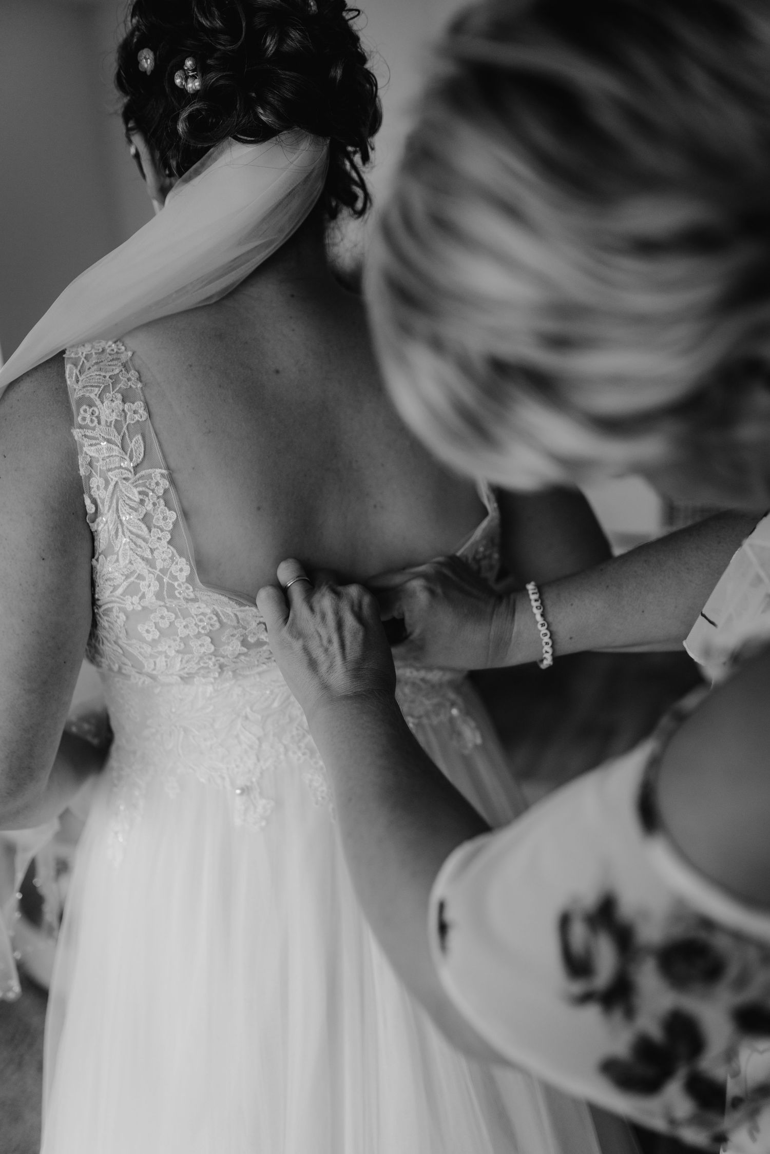 Helping a bride get dressed in a white lace wedding gown shown in black and white.