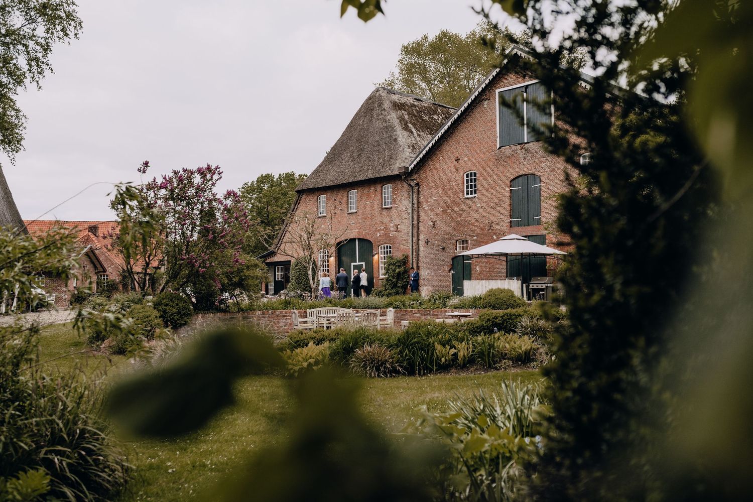 A charming brick farmhouse wedding venue surrounded by lush gardens and greenery.