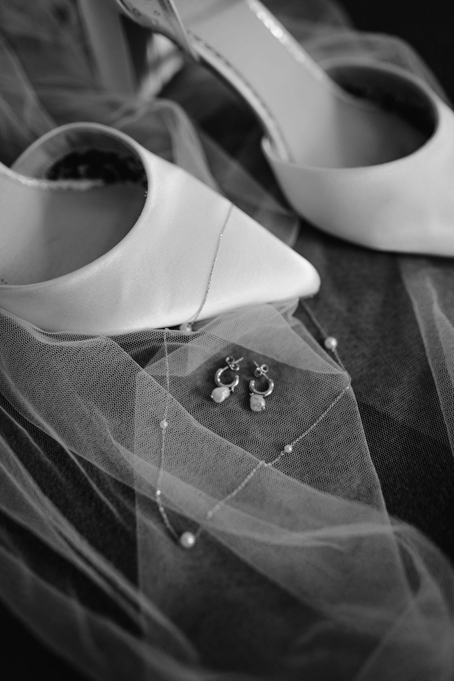 White bridal shoes and jewelry arranged with delicate tulle veil in an elegant black and white composition.