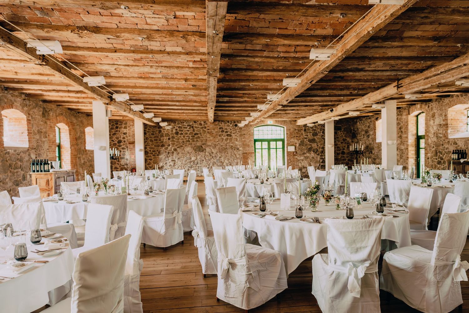 Rustic wedding reception venue with white-clothed tables and wooden beam ceiling.