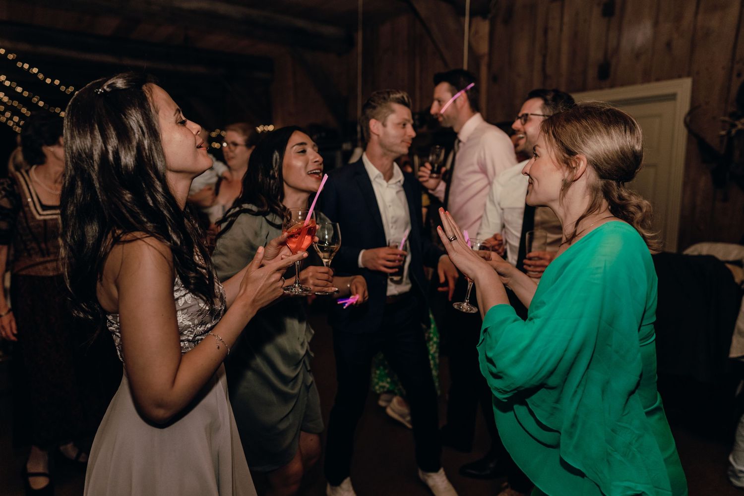 Wedding guests enjoying drinks and conversation at a dimly lit barn reception.