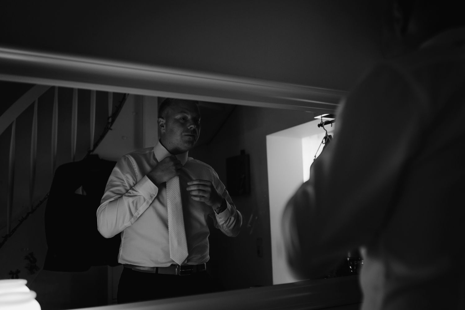Black and white photo of person fixing tie and checking reflection in a mirror.
