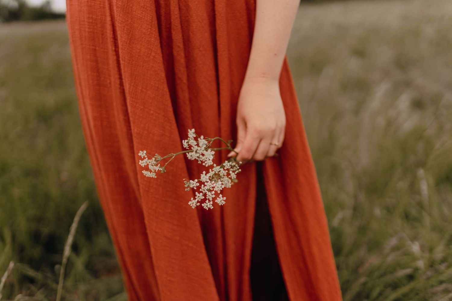 A person in an orange flowy dress walks through a sunlit field of tall grass during golden hour.