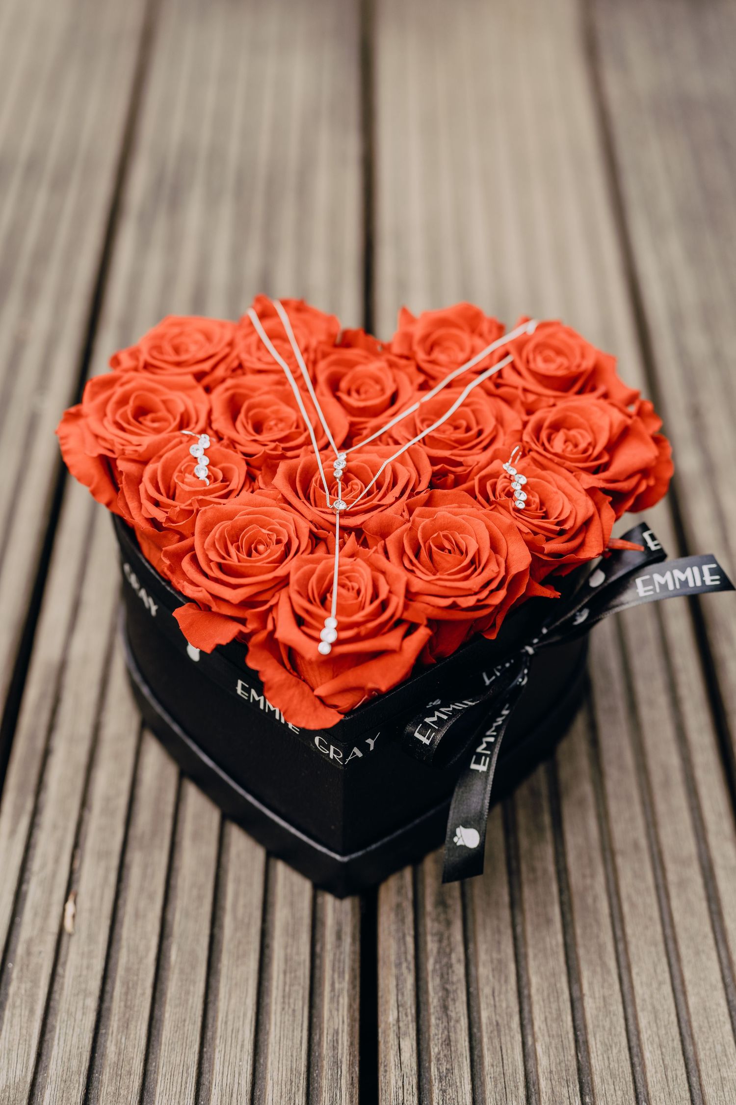 Beautiful red roses arranged in heart shape inside black gift box on wooden deck background.