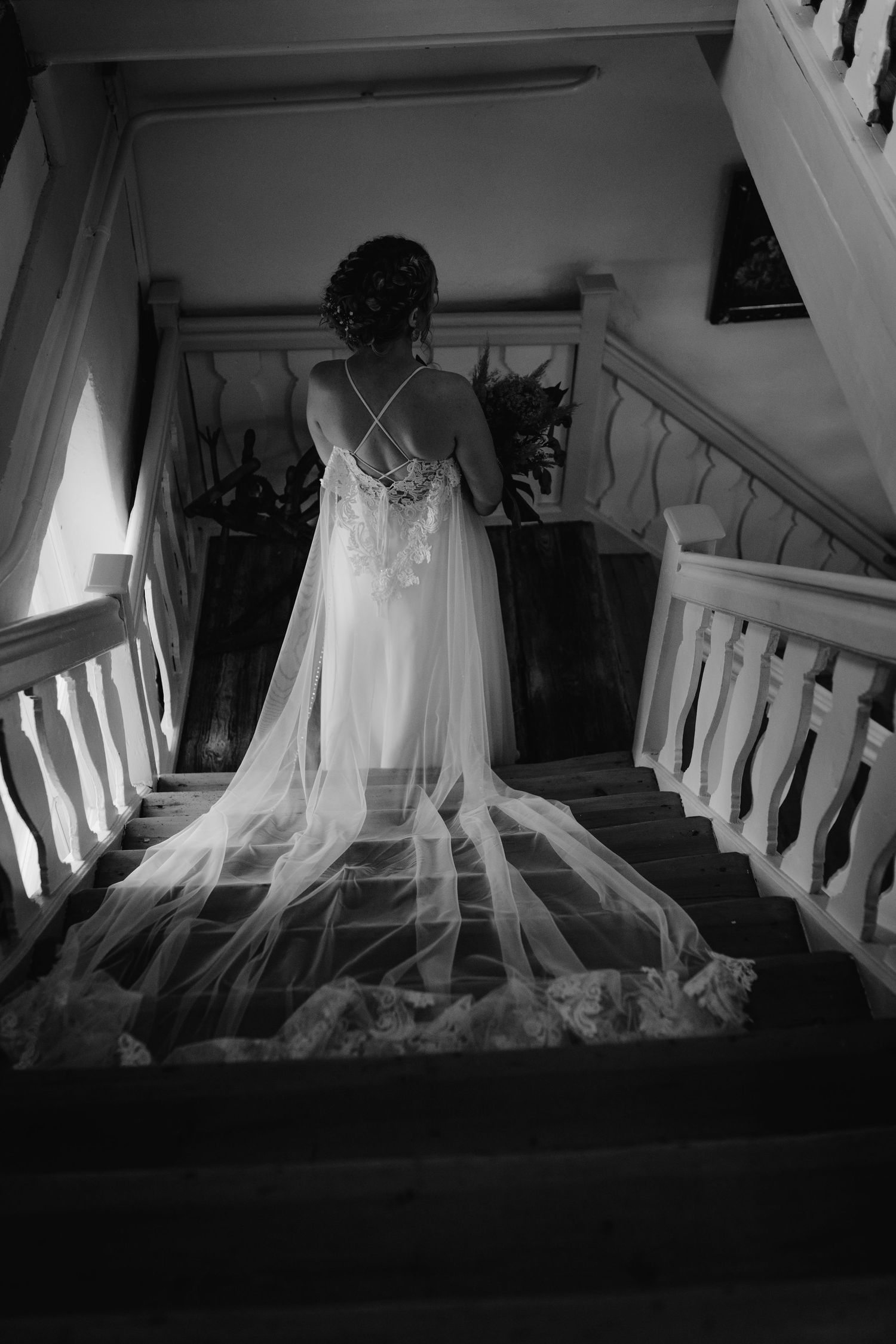 A dramatic black and white photograph shows a bride in a flowing gown with a long train descending an elegant staircase.