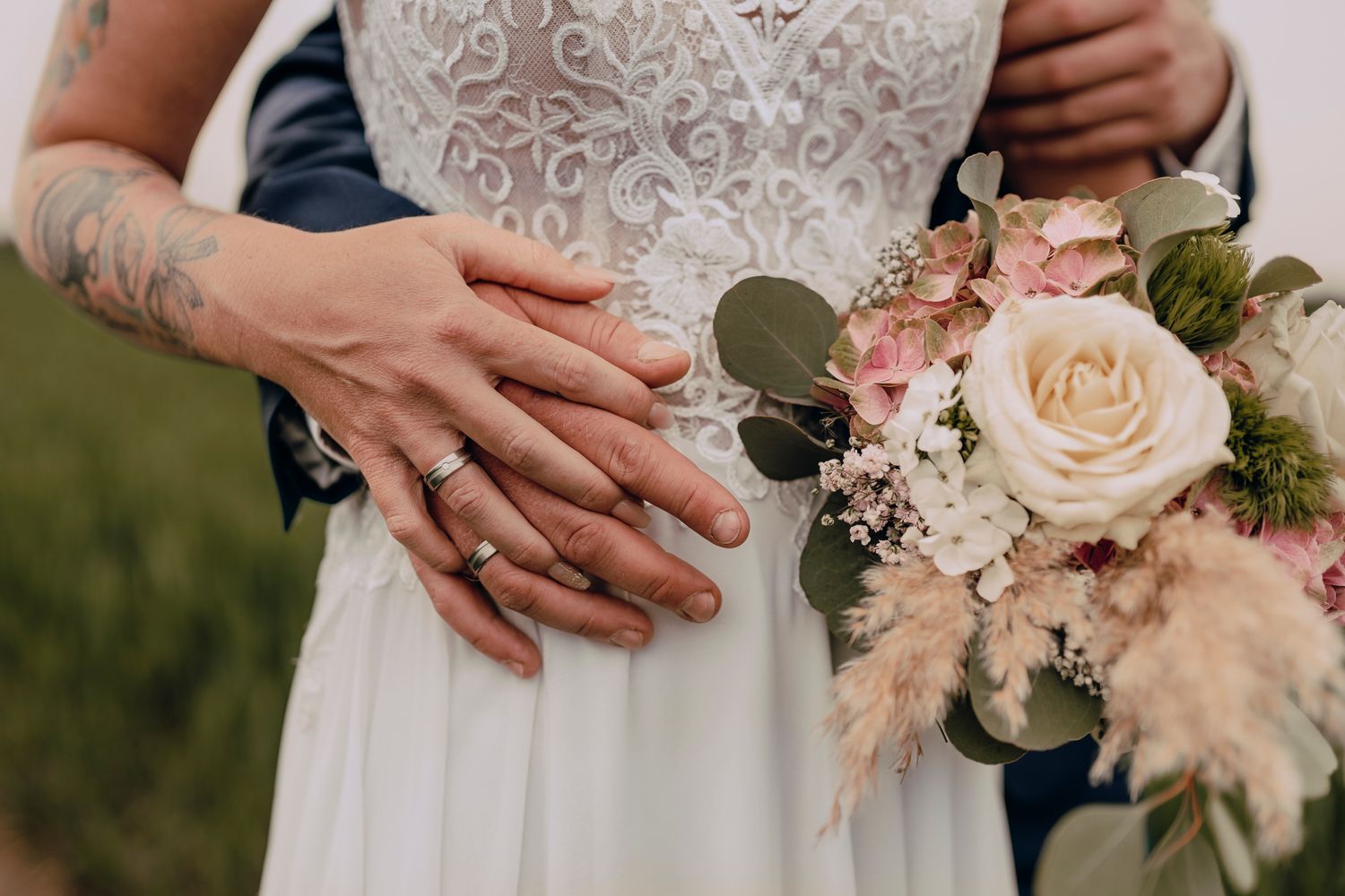 Close up of hands holding a romantic bridal bouquet with blush roses and eucalyptus against a white dress.