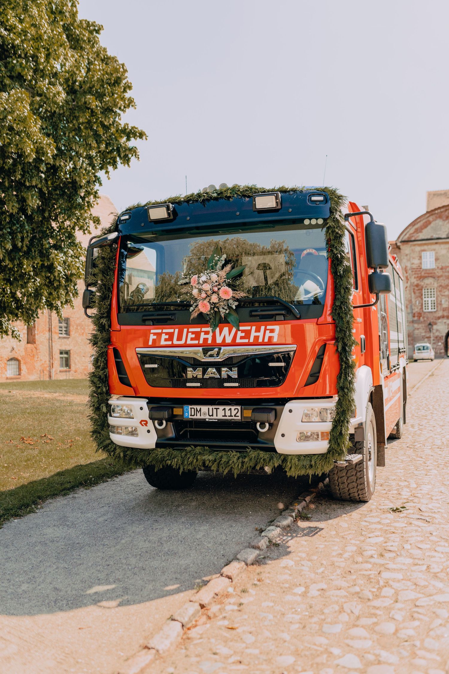 A red German fire truck (Feuerwehr) parked on a cobblestone street next to historic buildings.