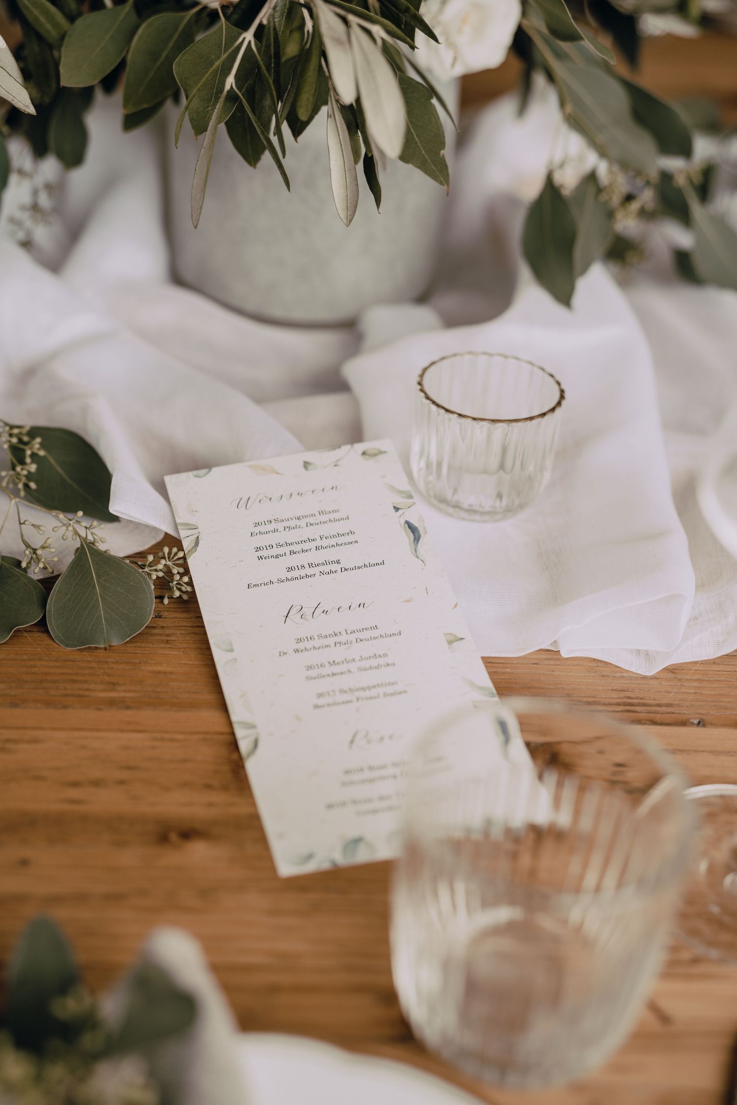 Elegant wedding reception table setting with white menu cards, greenery and wooden details.