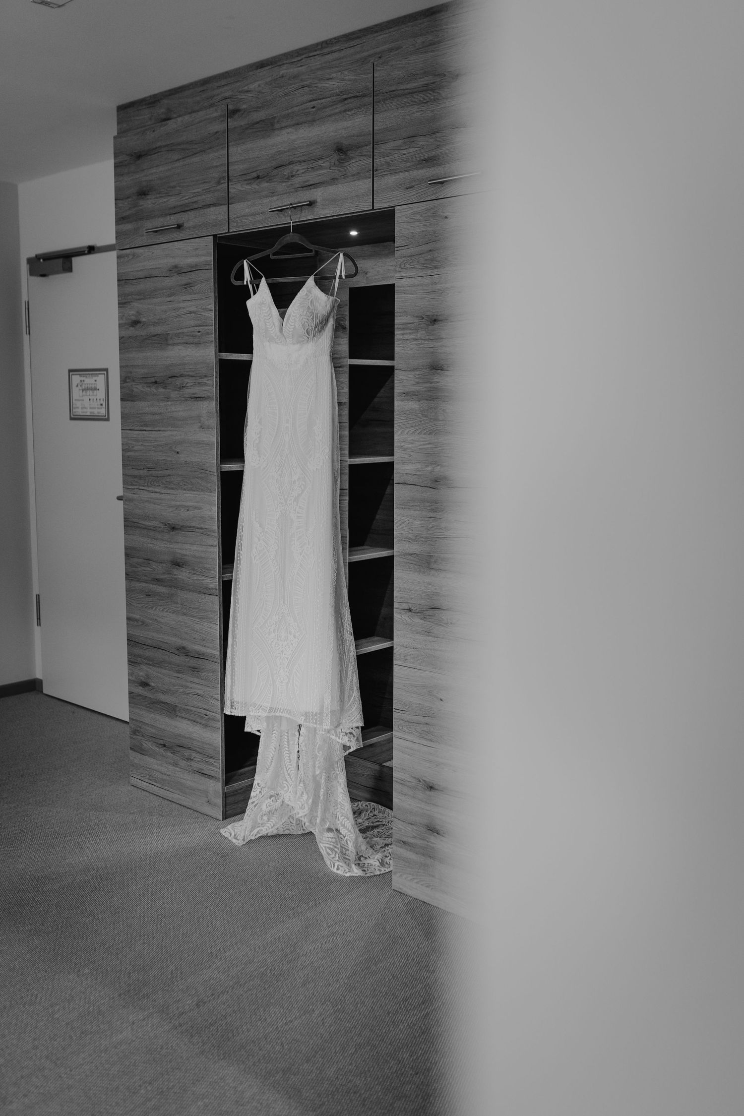 An elegant white lace wedding dress hangs on display against a wooden paneled wall.