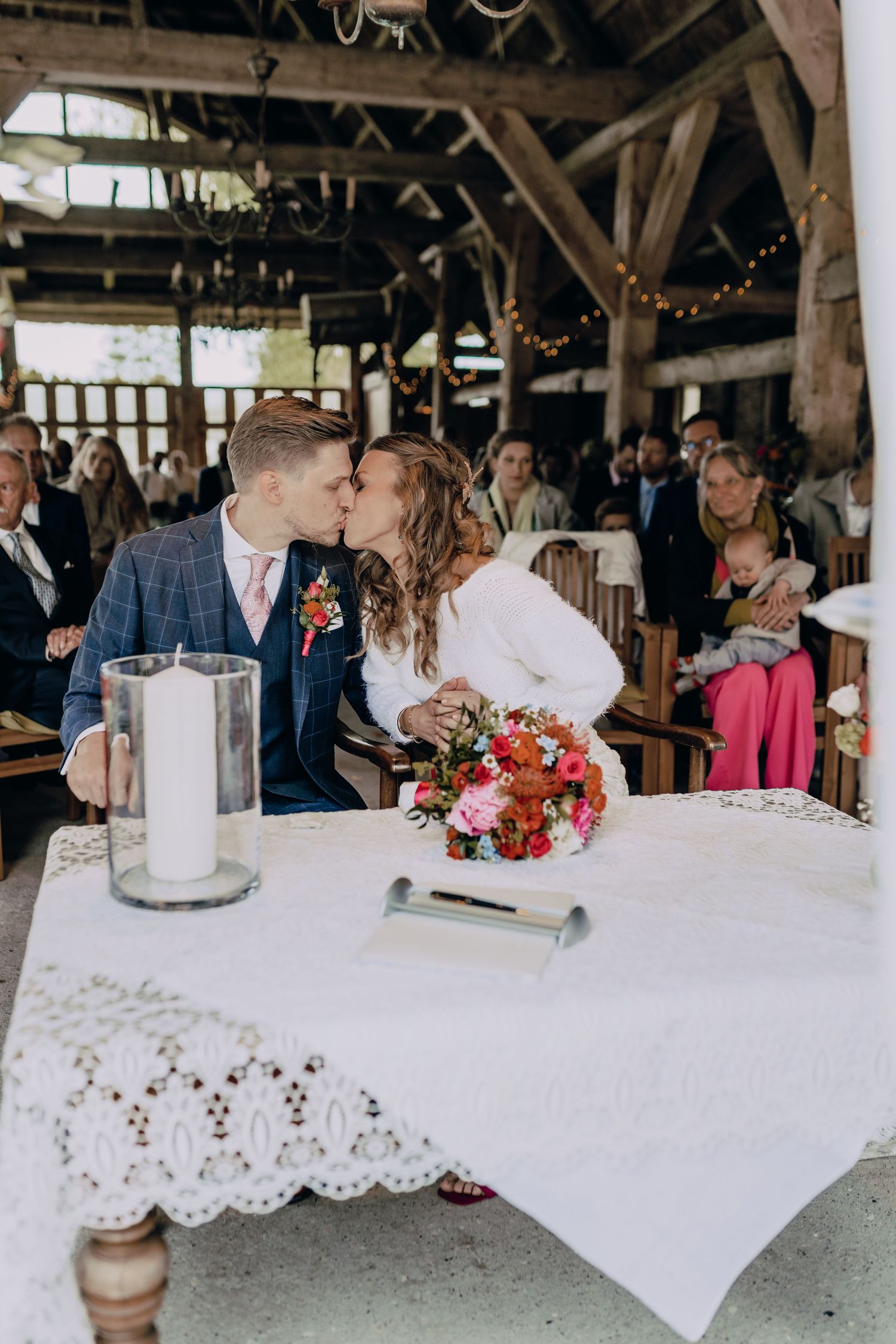 Romantic wedding reception scene in a rustic barn with white lace tablecloths and floral decorations.
