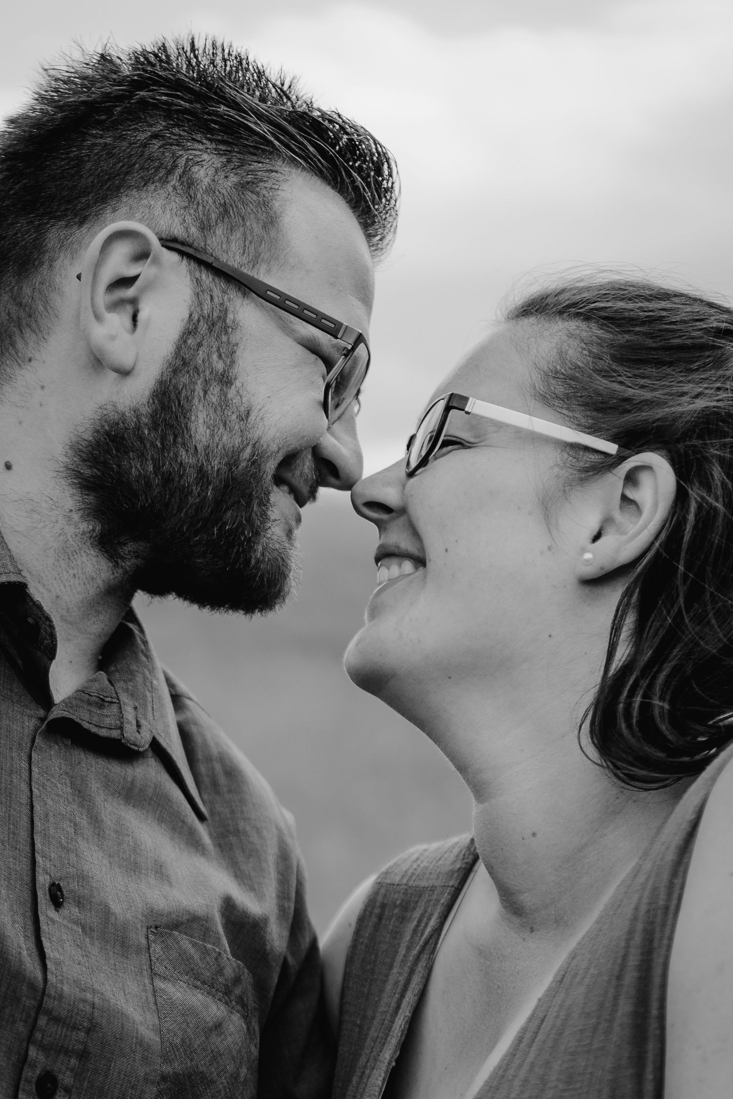 Close up black and white portrait of a couple wearing glasses smiling at each other in an intimate moment.