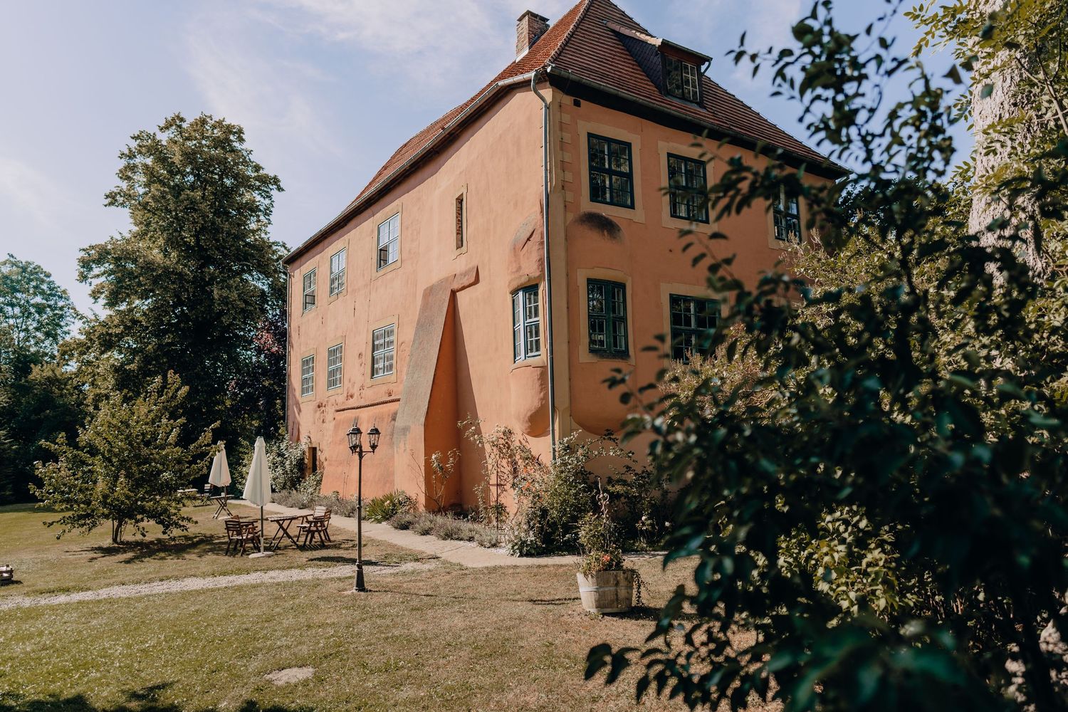 Large rustic peach-colored manor house with multiple windows surrounded by green trees.