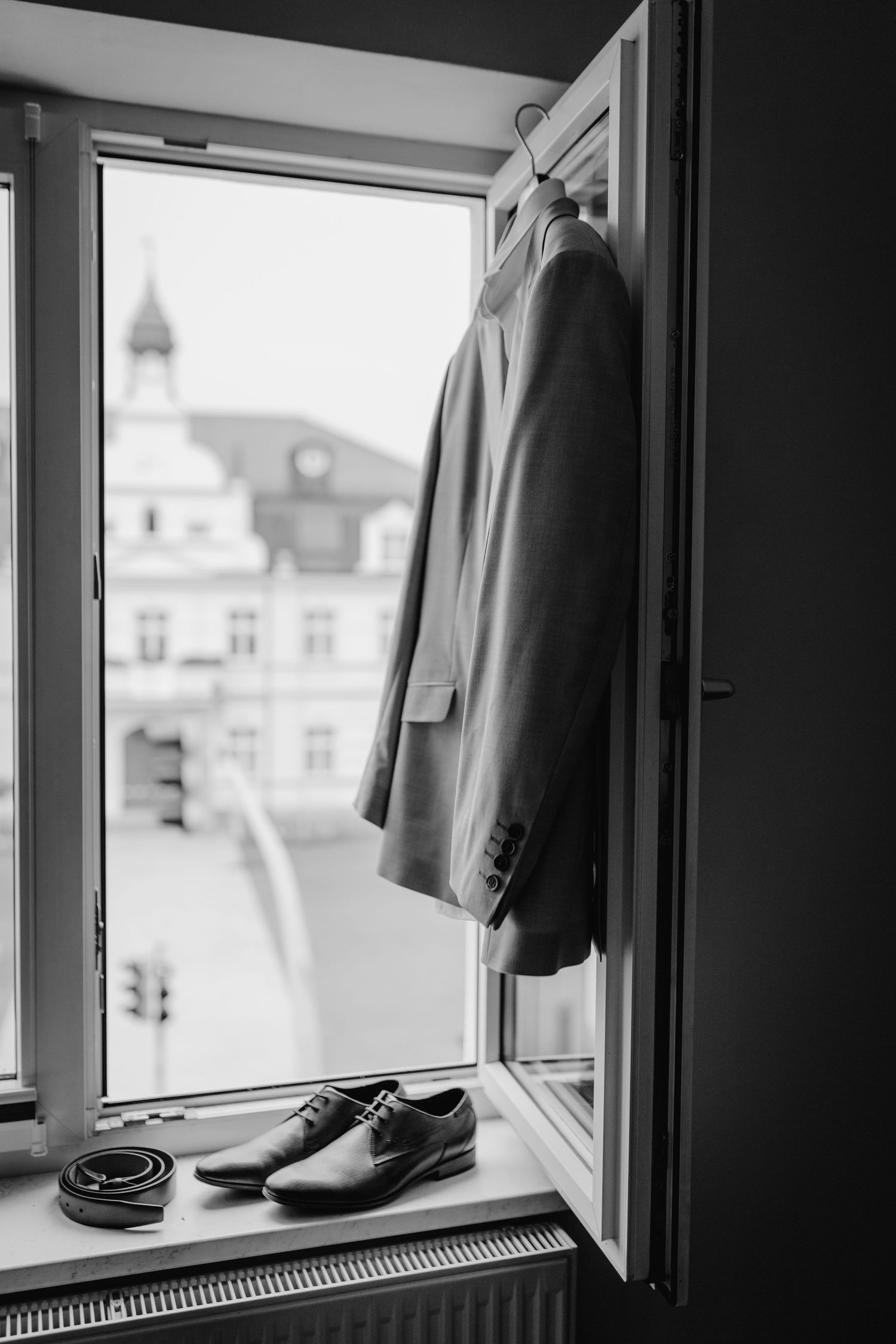 A formal suit jacket and dress shoes arranged by a window with city buildings visible in the background.