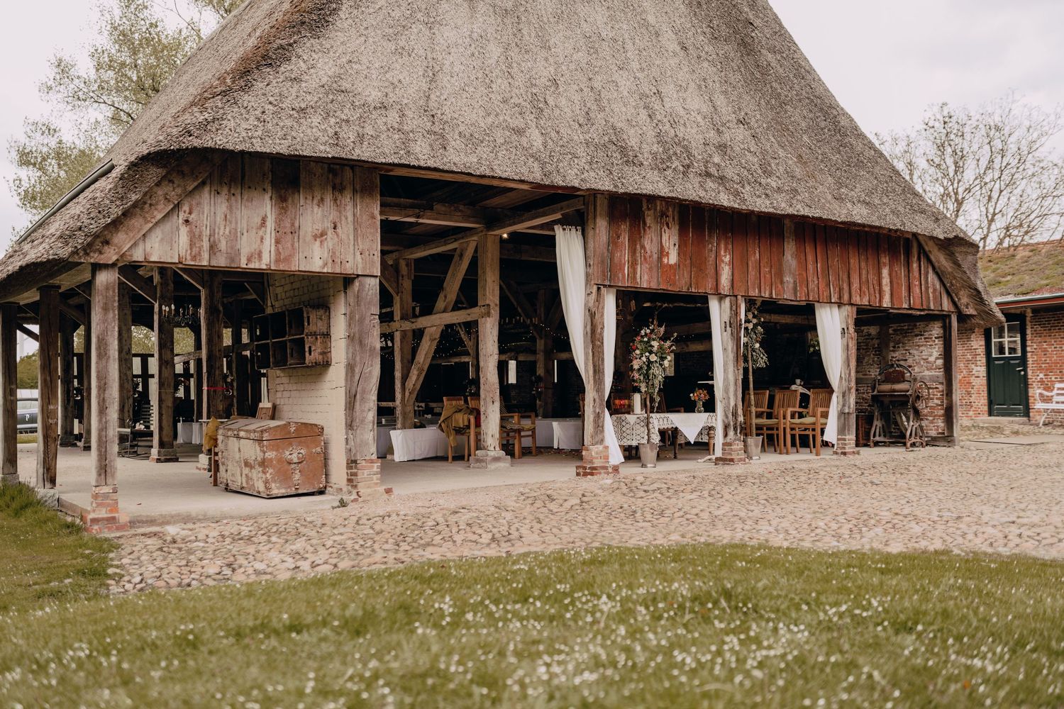 Rustic thatched-roof barn venue with outdoor seating and white curtains flowing in the breeze.