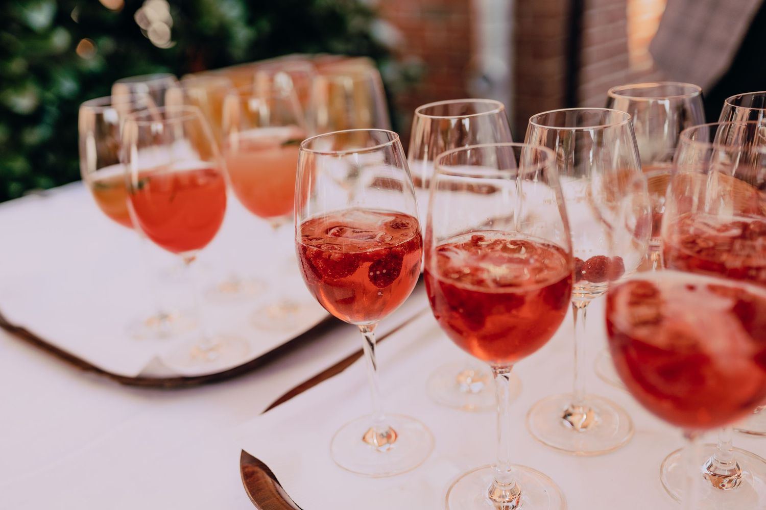 Several glasses of rose wine arranged in a row on a white tablecloth at an outdoor event.