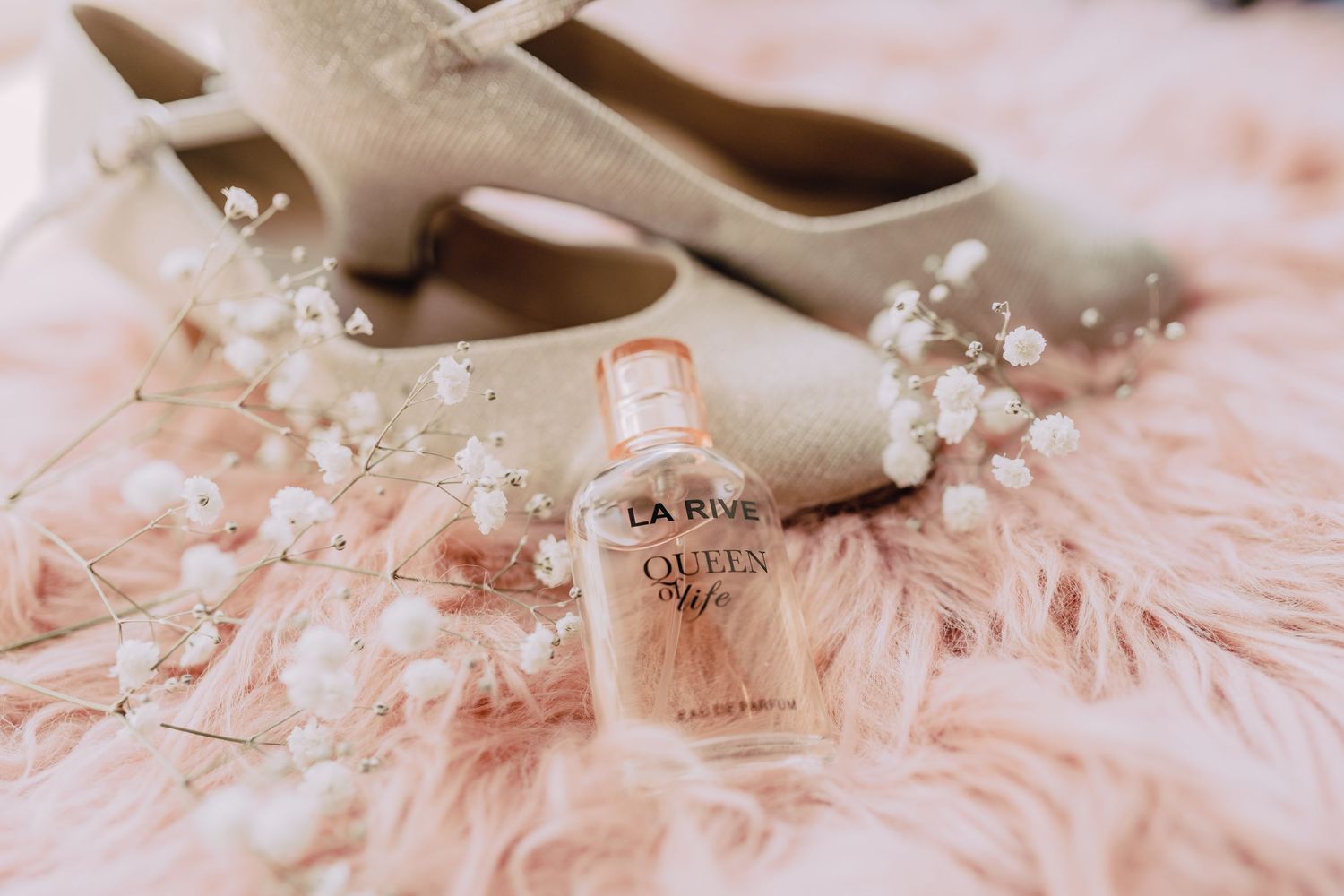 Sparkly pink feminine wedding shoes arranged with delicate pearls and soft feather details on a light surface.
