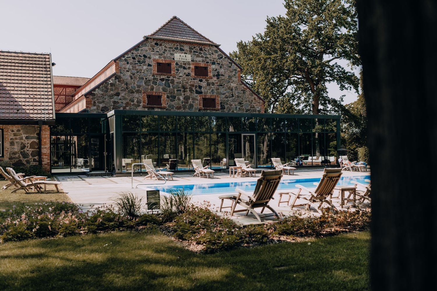 Stone building with swimming pool and lounge chairs in garden setting.