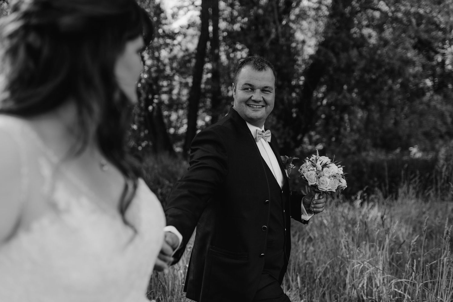 A candid wedding moment captured in black and white showing joyful expressions in an outdoor setting.