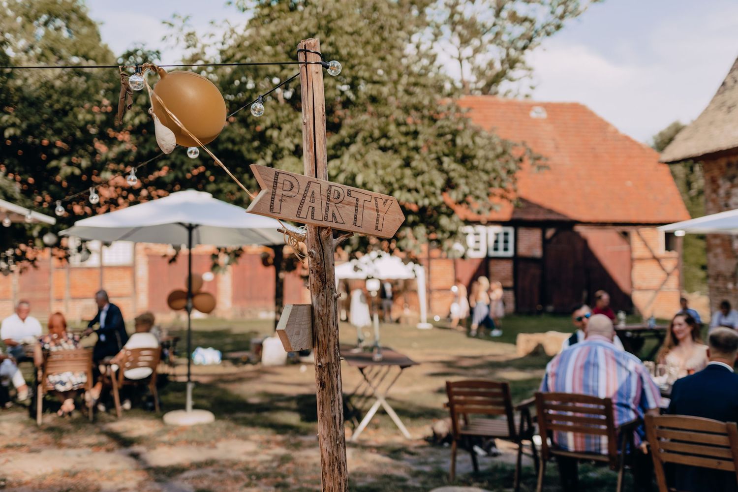 Outdoor wedding venue with wooden decorations and guests seated at tables under open sky.