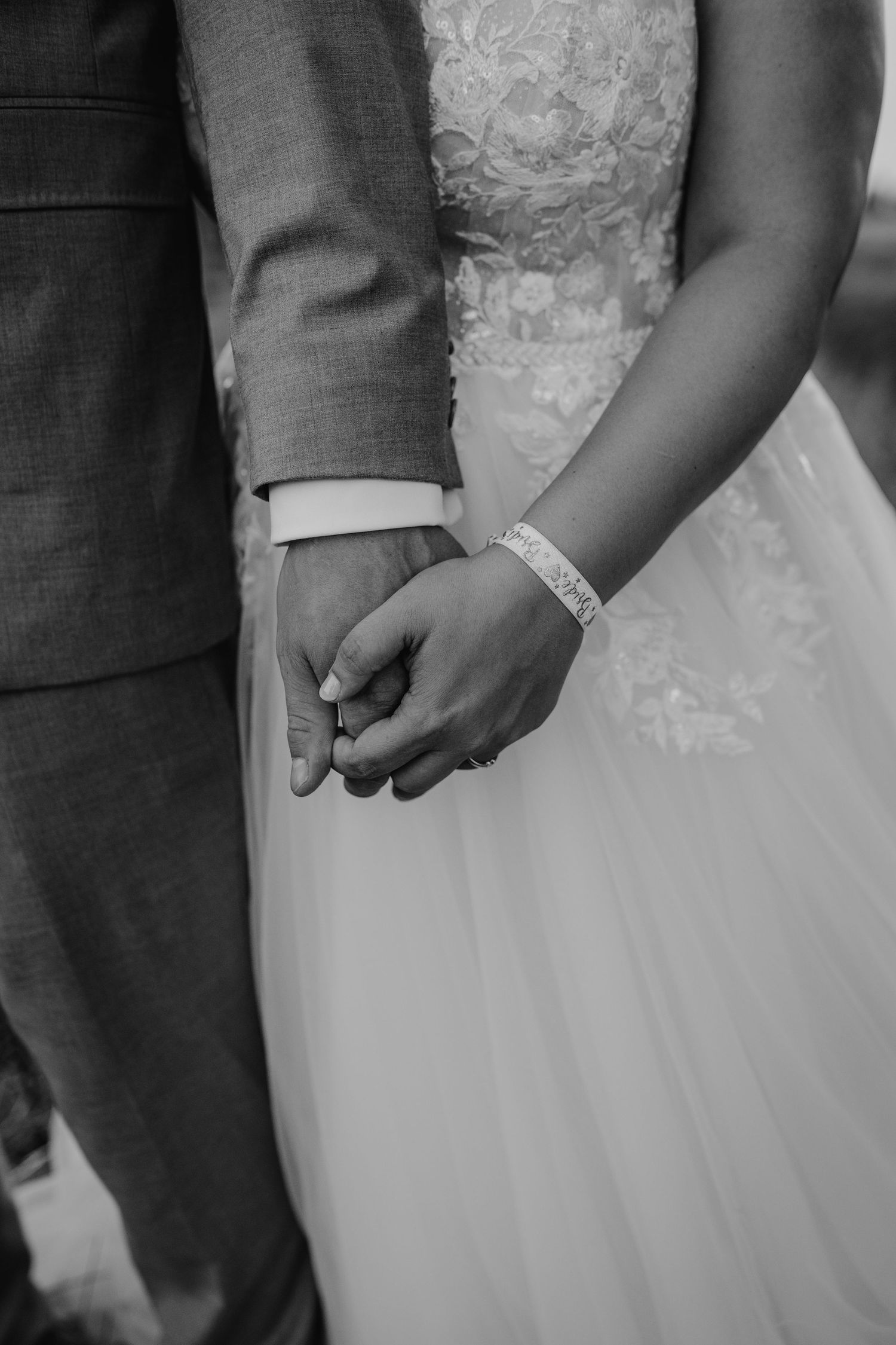 Close-up view of a bride and groom holding hands, showcasing wedding rings and formal attire.