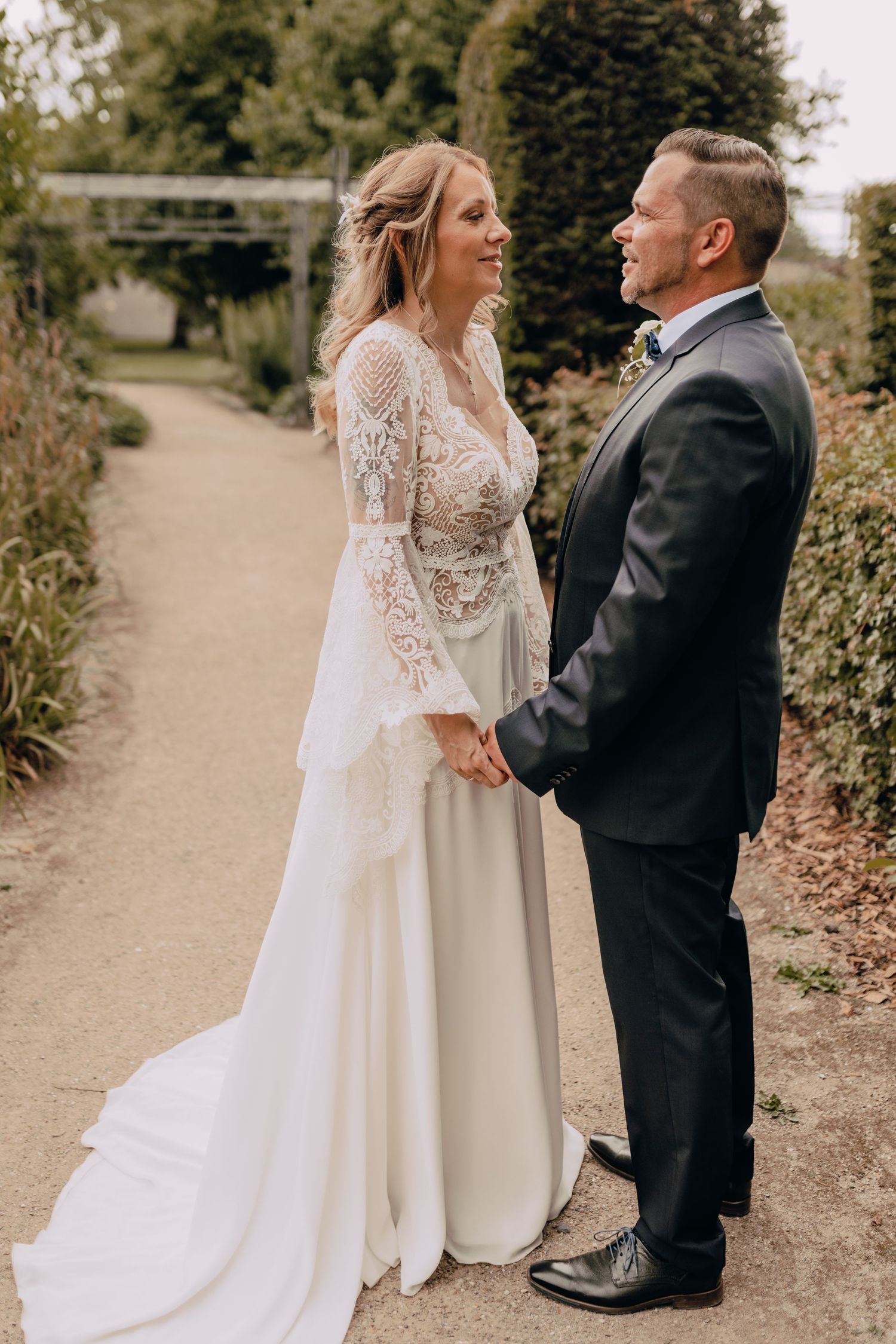 A couple in wedding attire stands together on a garden path during their outdoor autumn wedding ceremony.