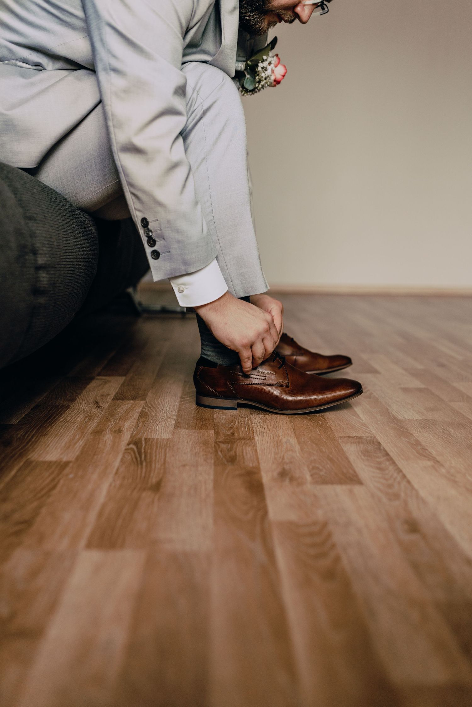 Brown leather dress shoes being put on with a light grey suit visible.