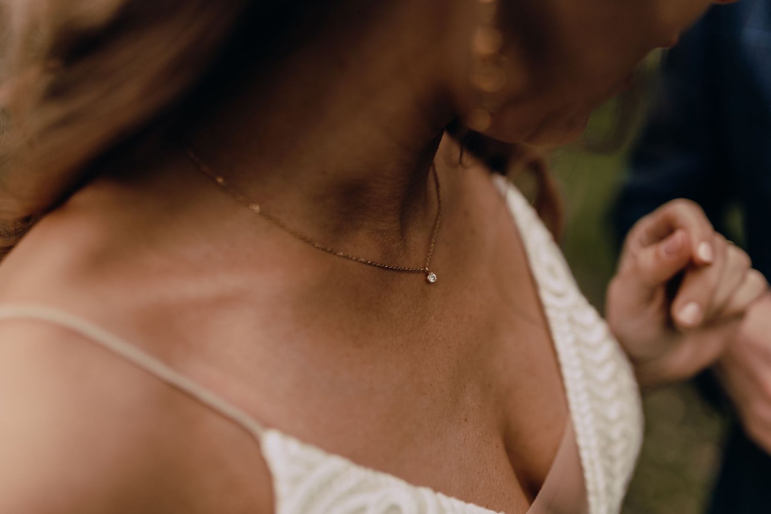 Detail shot of delicate necklace and white lace wedding dress bodice.