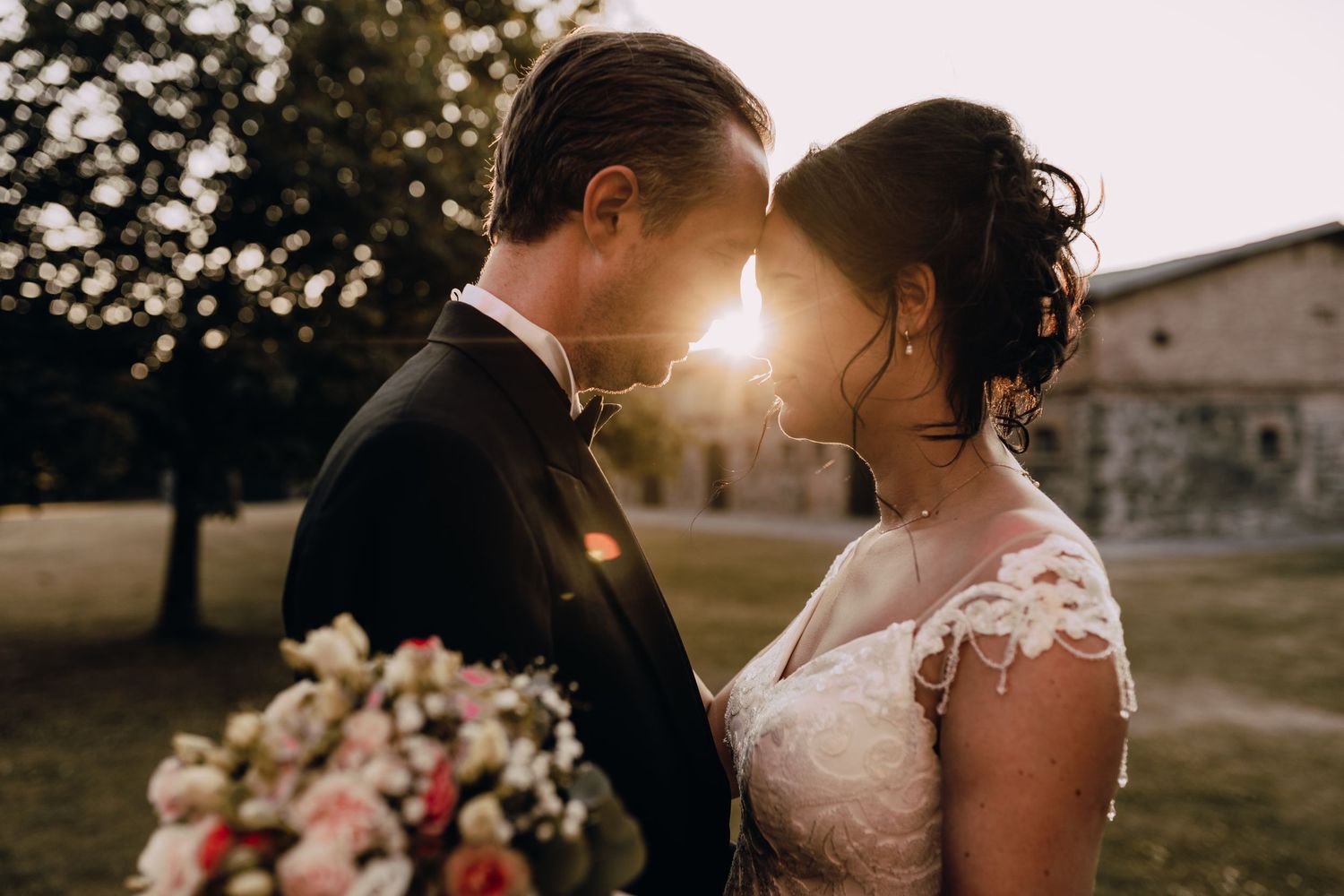 Romantic sunset portrait of newlyweds with rustic building in background.