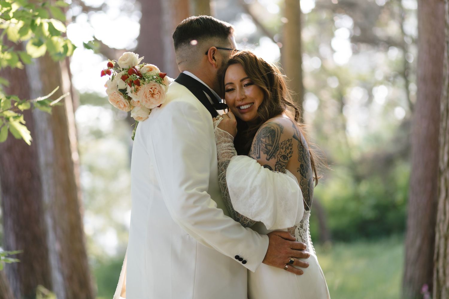 A romantic forest wedding portrait with soft sunlight filtering through pine trees.