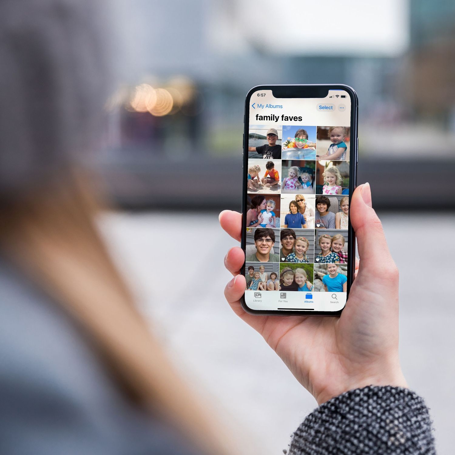 A person holding a smartphone camera roll filled with a photo gallery grid of many family pictures to choose from.