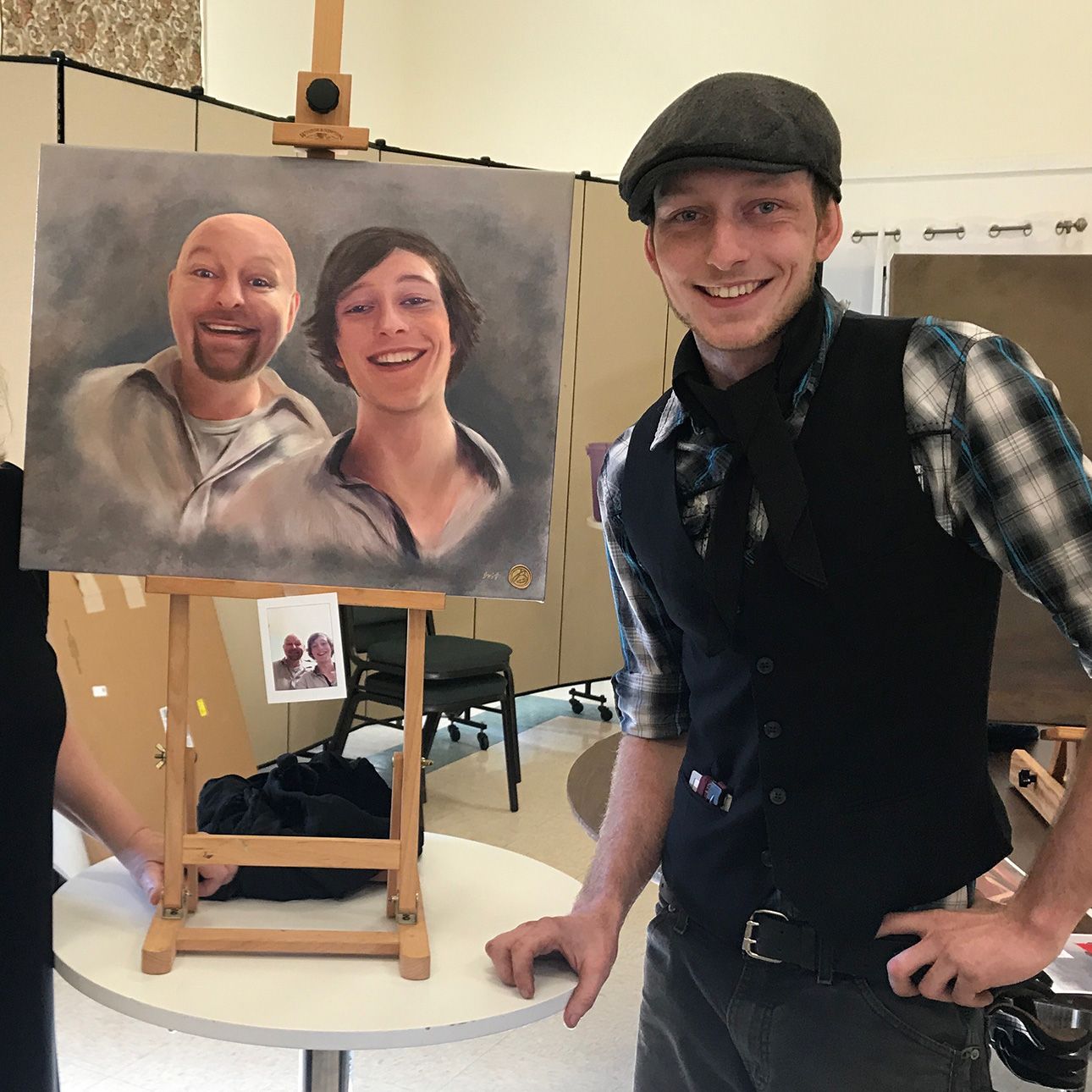 Artist stands proudly next to their completed portrait painting on an easel in a studio setting.