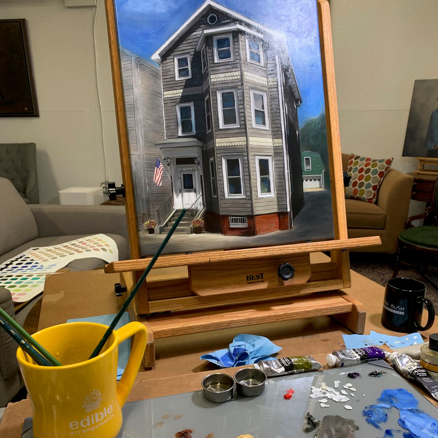 In the studio, a house portrait painting being worked on, on the easel. Paints, palette and brushes in view.