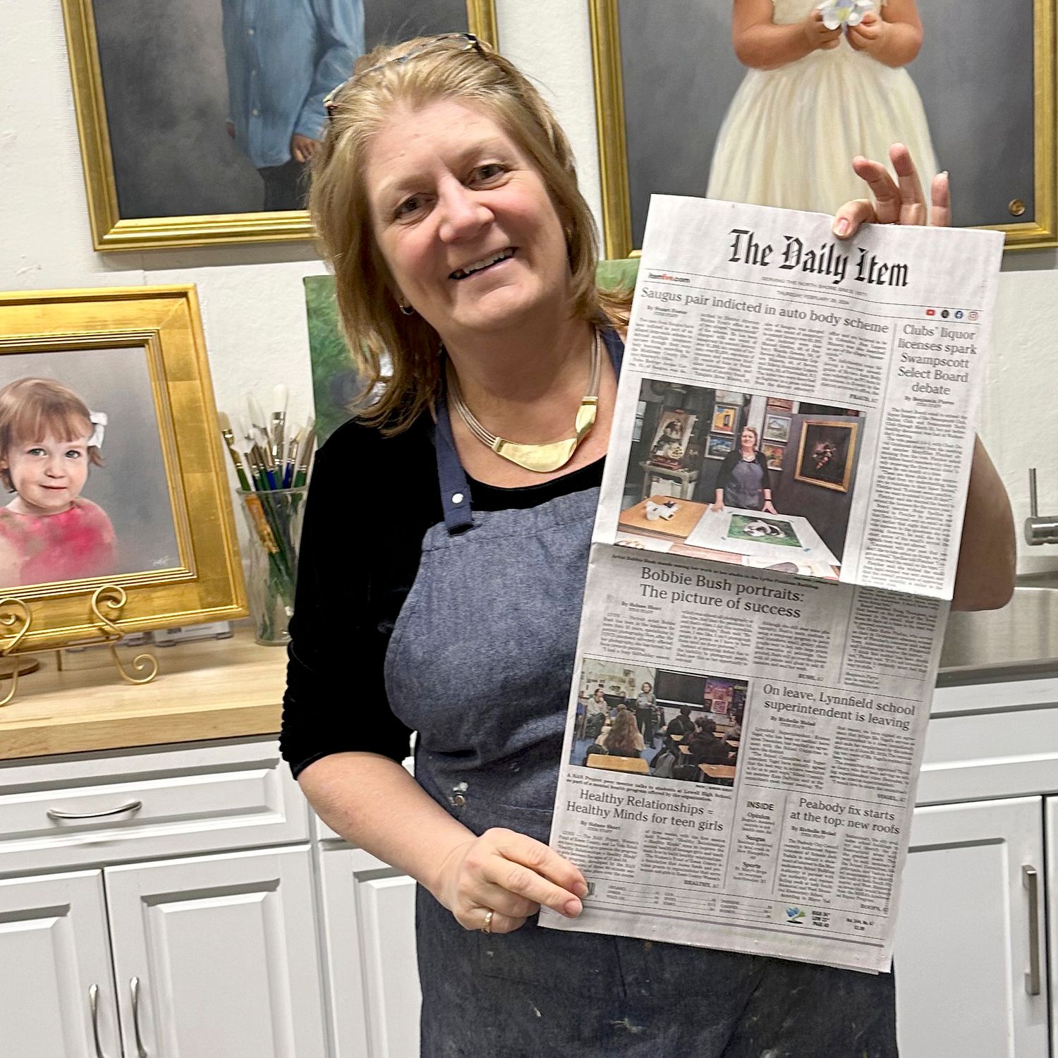 Bobbie Bush holding the front page of the Lynn Daily Item newspaper with the feature article about her studio on page one.