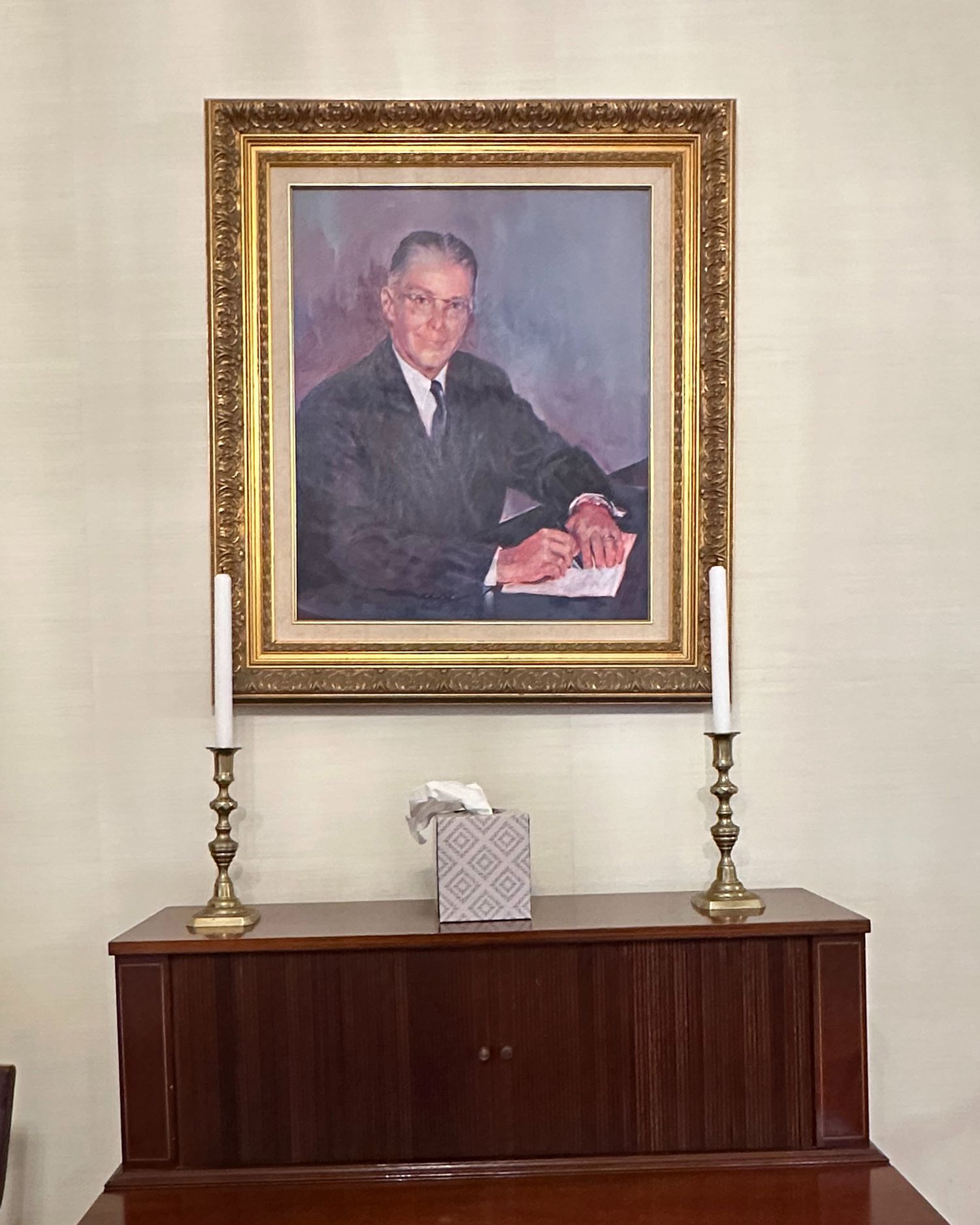 An ancestor's portrait painting in gold frame mounted above dark wooden cabinet with brass candlesticks.