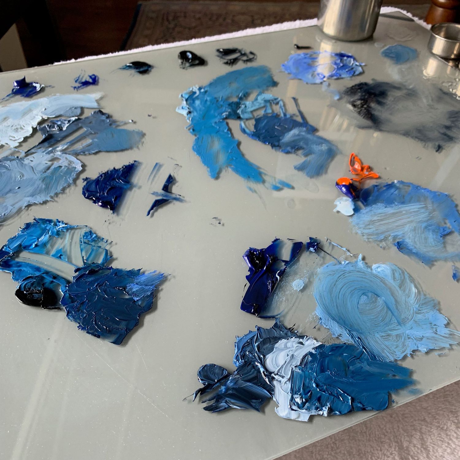 Paint palette showing various shades of blue oil paints being mixed on a grey surface.