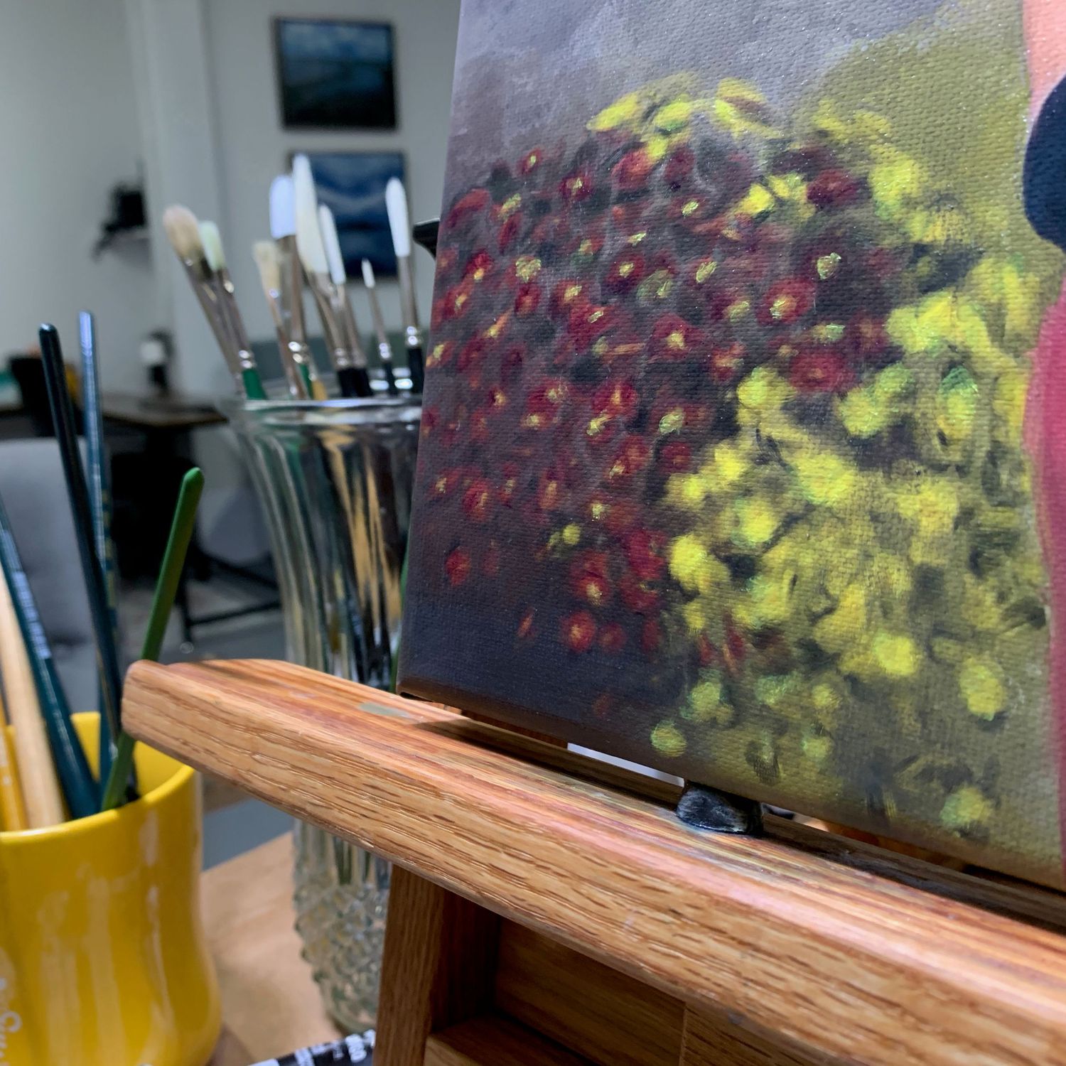 Paint brushes next to canvas on the easel. Detail of painting shows red and yellow mums.