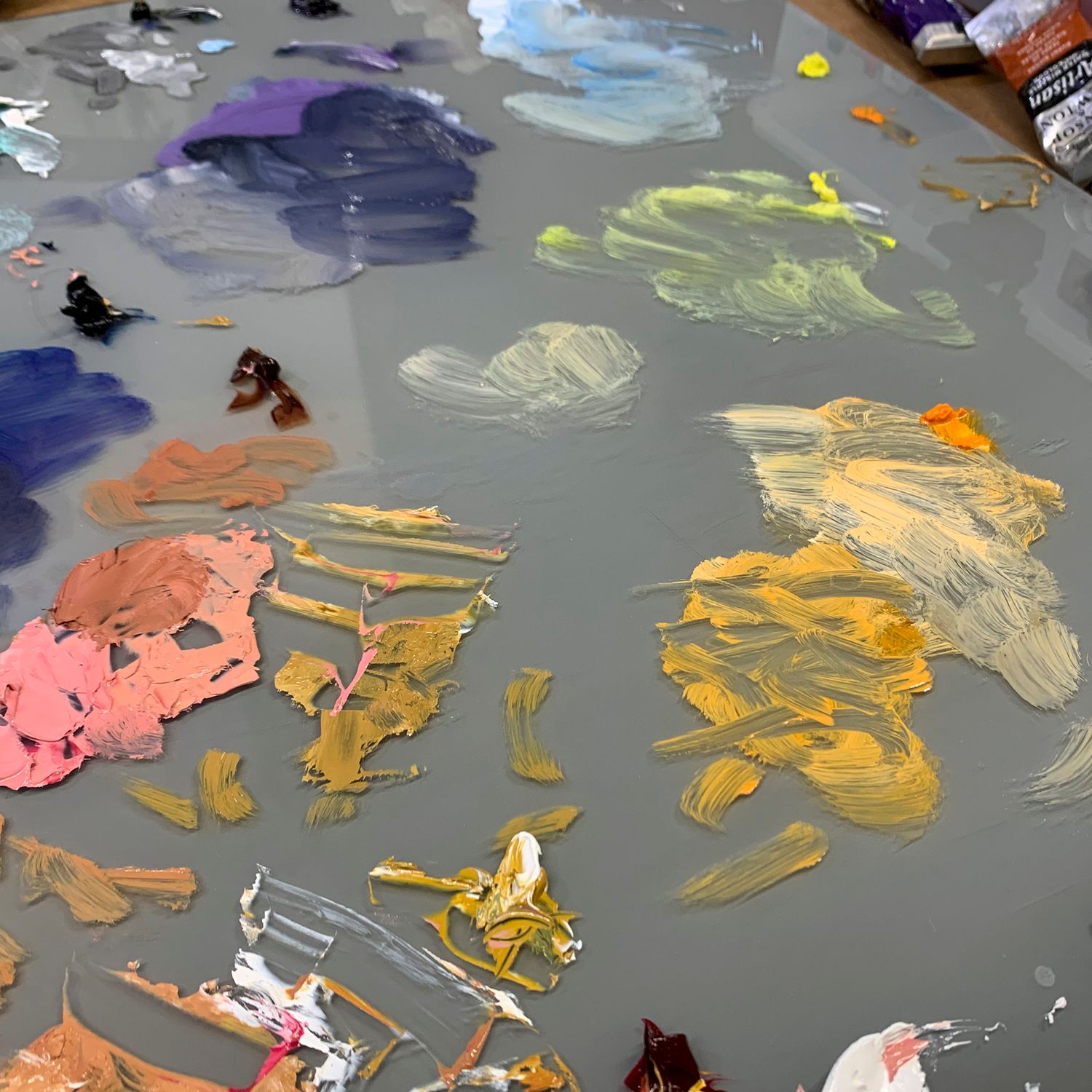 Artist's paint palette with mixed colors of pink, yellow, and purple spread across gray surface.