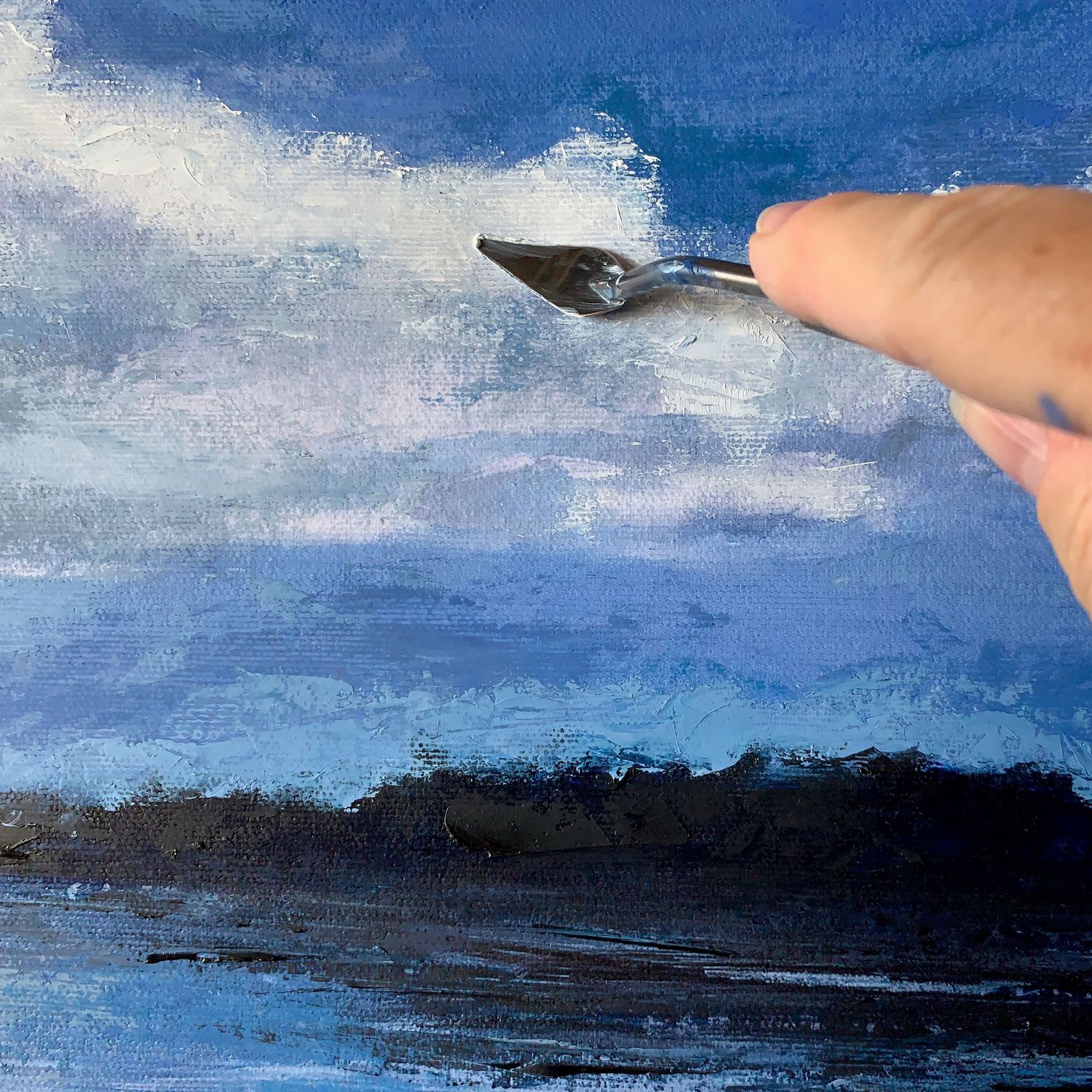 Using a palette knife on a landscape, adding oils to the clouds in the sky over a dark coastline and blue waters.