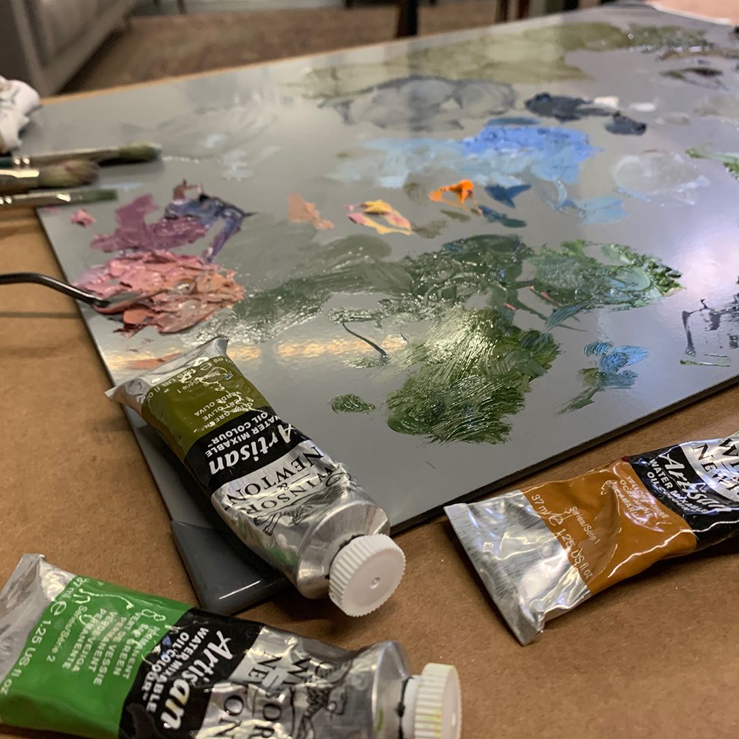Artist's palette with various paint colors and tubes of oil paint scattered on work surface.