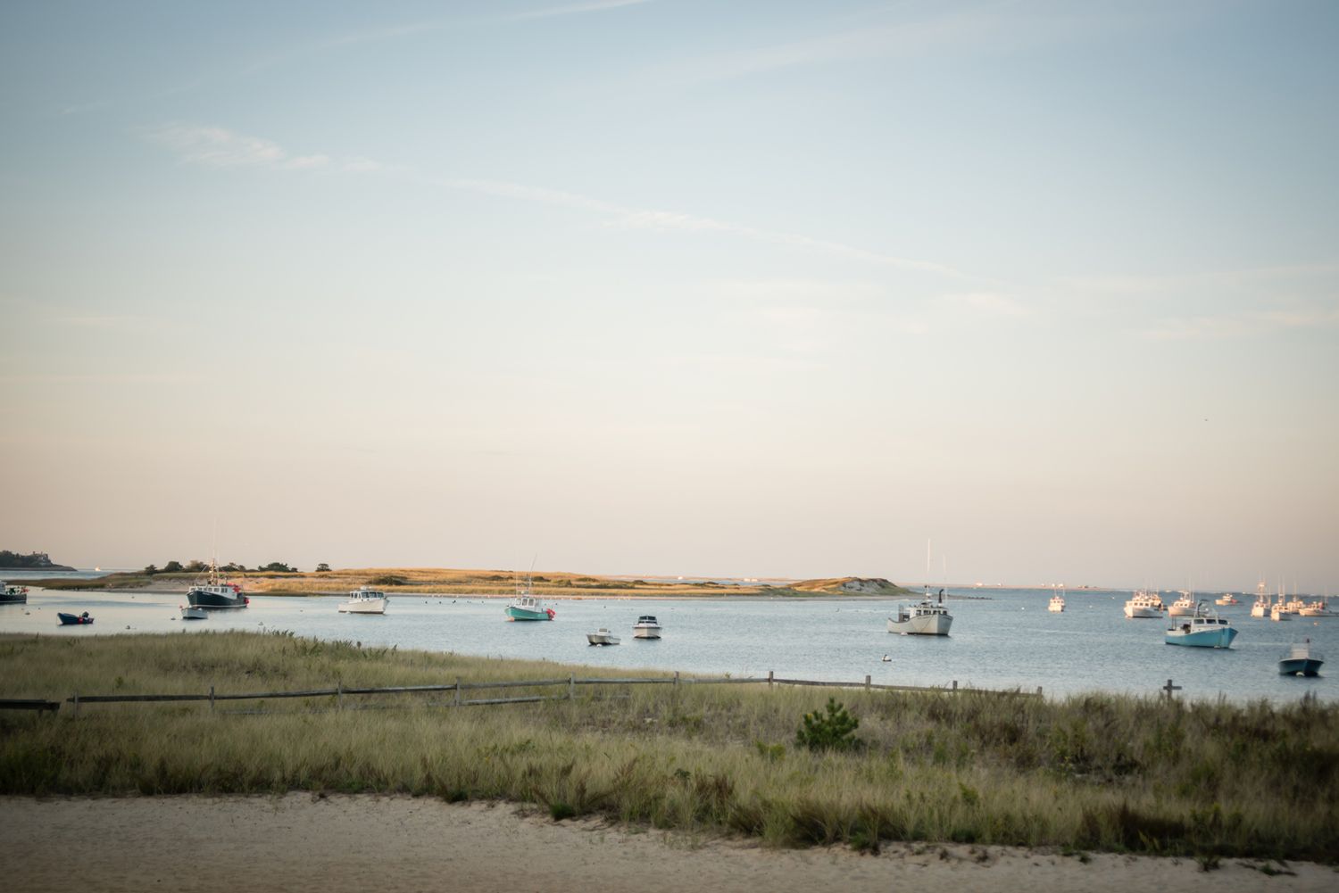 Peaceful harbor view with boats moored in blue water surrounded by sandy coastal grasslands. The view from a couple's wedding venue.