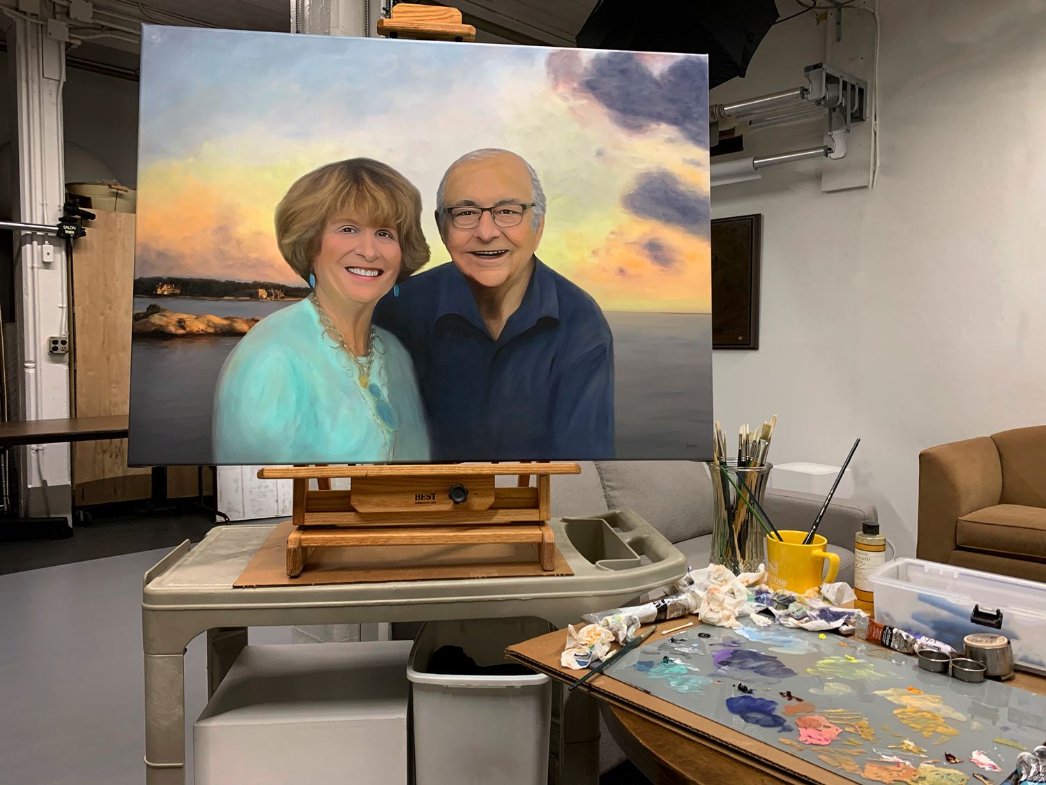 Portrait painting in progress on an easel with art supplies and palette on studio table.