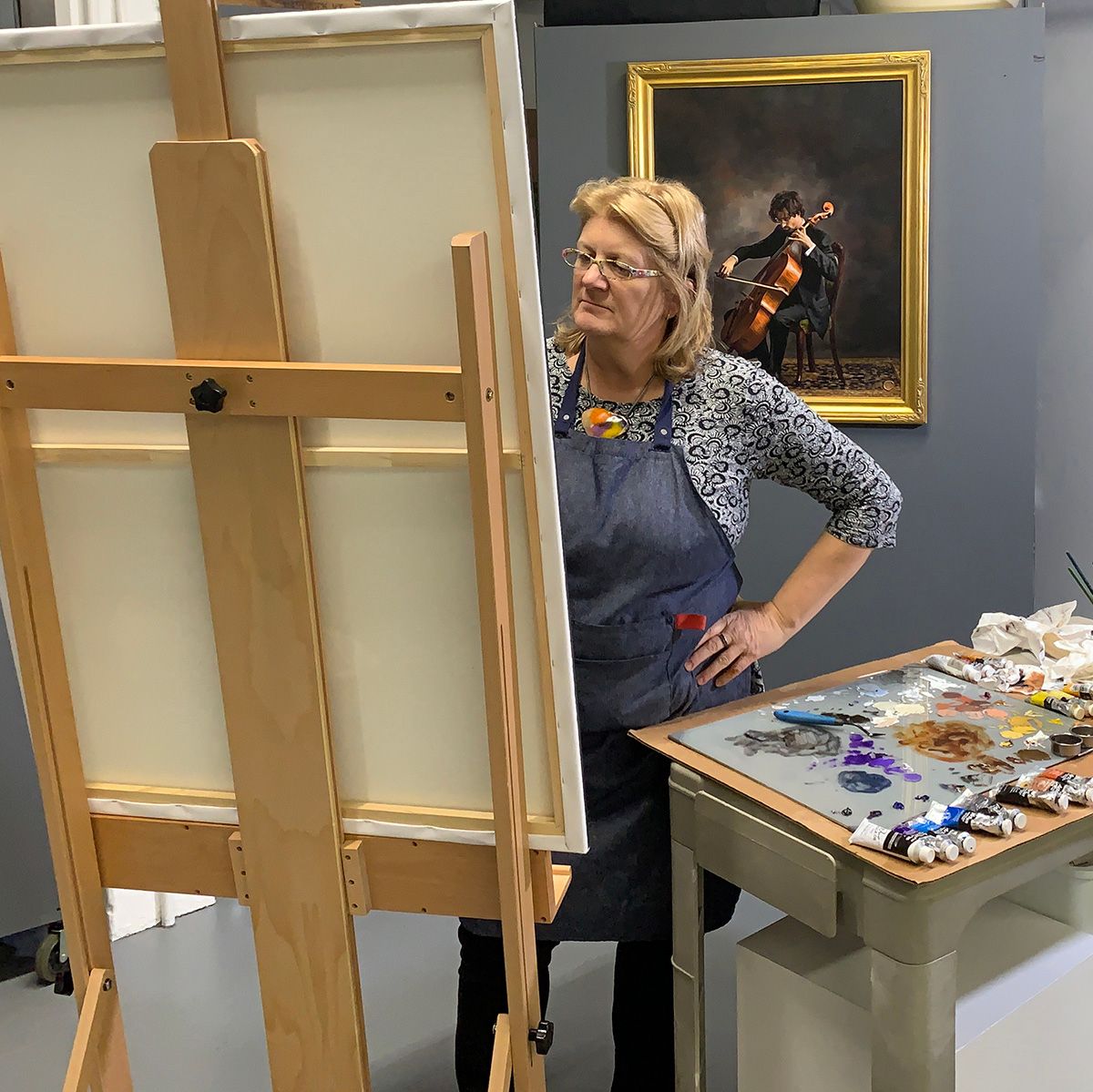 Artist Bobbie Bush standing at a wooden easel in her studio space.