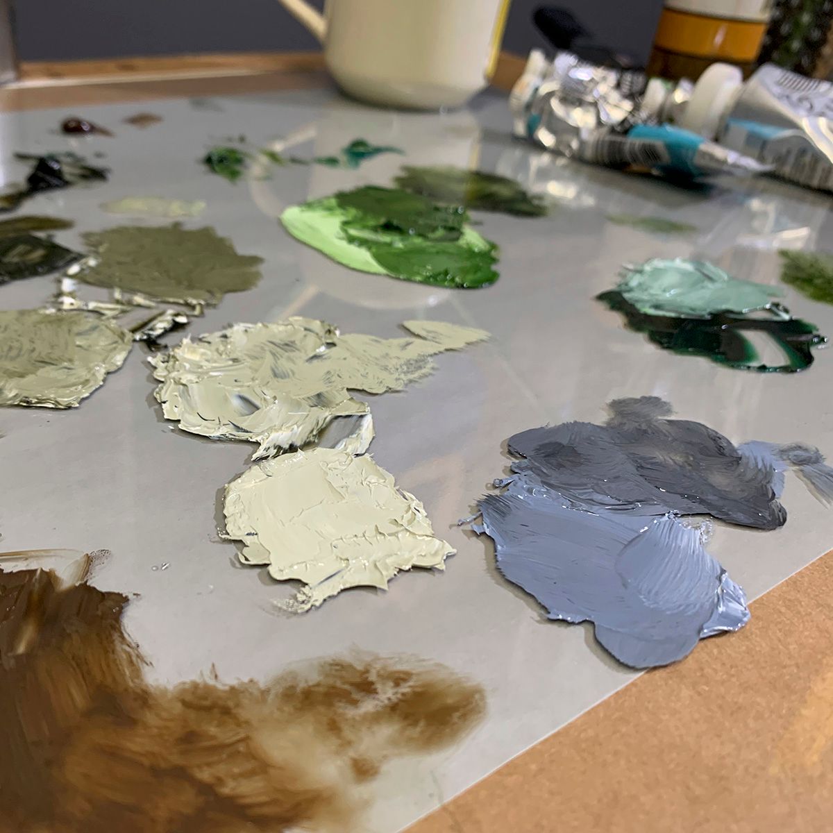 Artist's paint palette showing various mixed colors of oil paint in grey, green and blue tones.