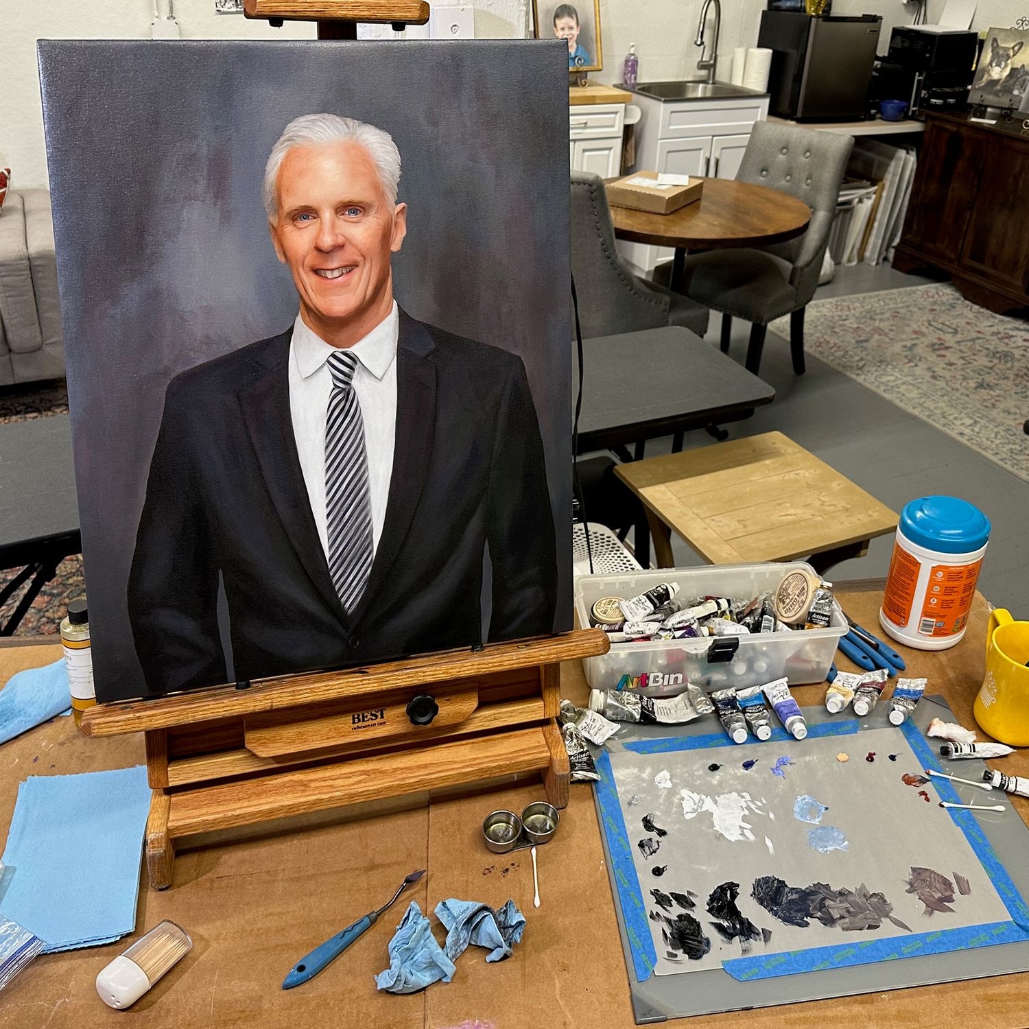Work in progress, in an artist's workspace with a memorial portrait of a gentleman on the easel.