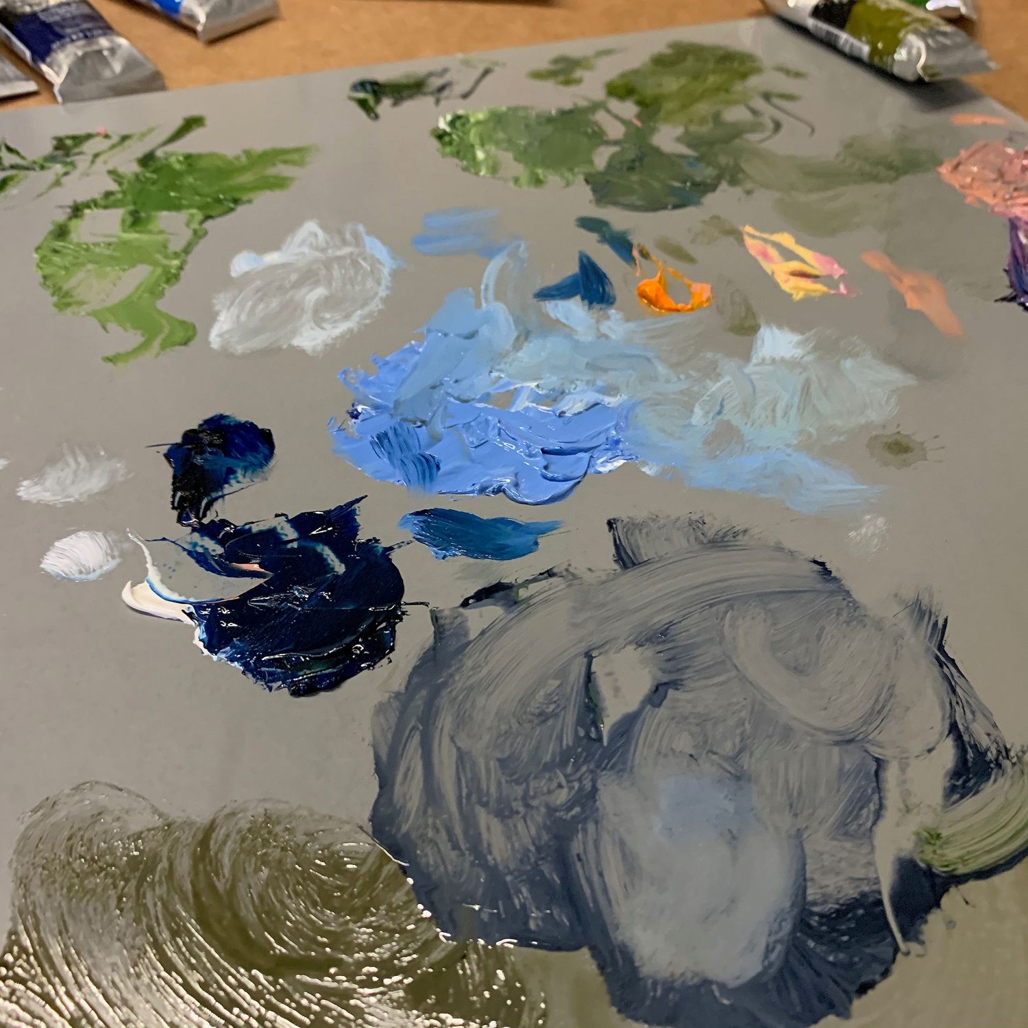 Artist's palette with various mixed oil paints in blues, greens, and grays.