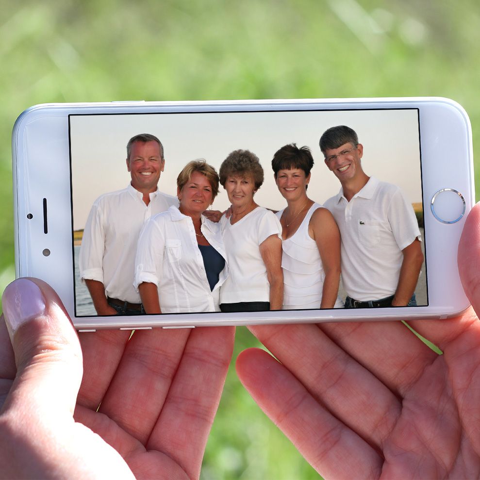 Holding up an iPhone displaying a group family photo. The center figure was used as a reference for a memorial painting.
